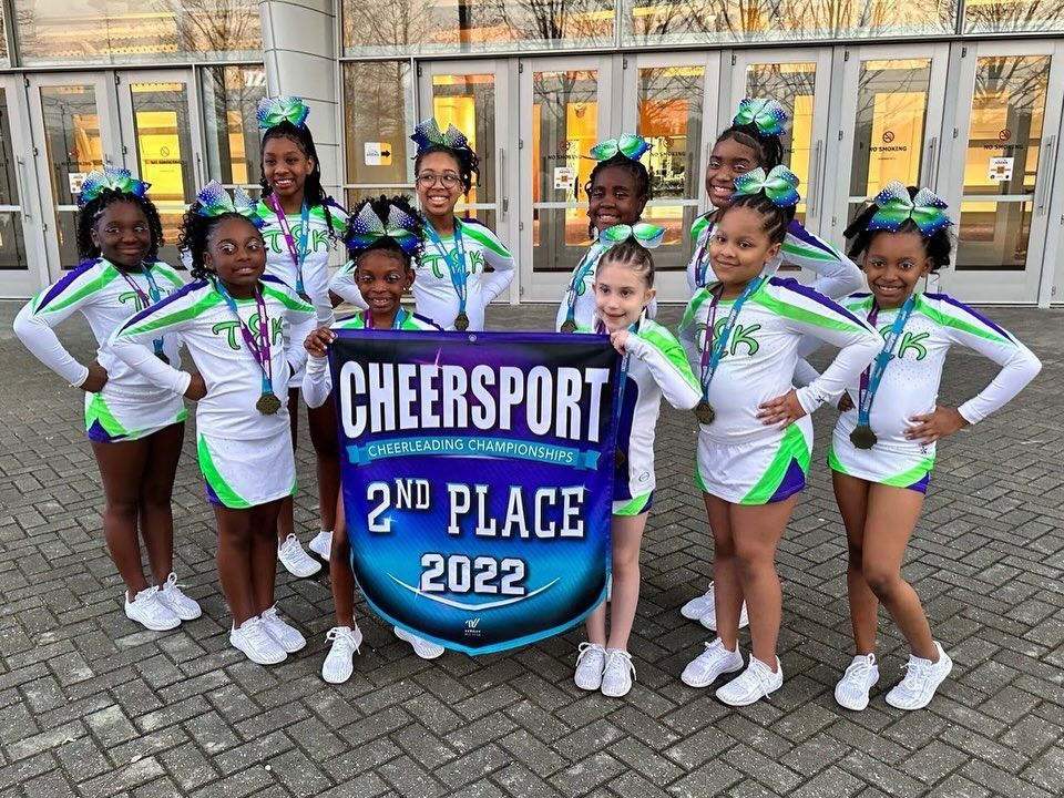 Cheer team poses with a “2nd Place 2022” trophy banner outside a building.