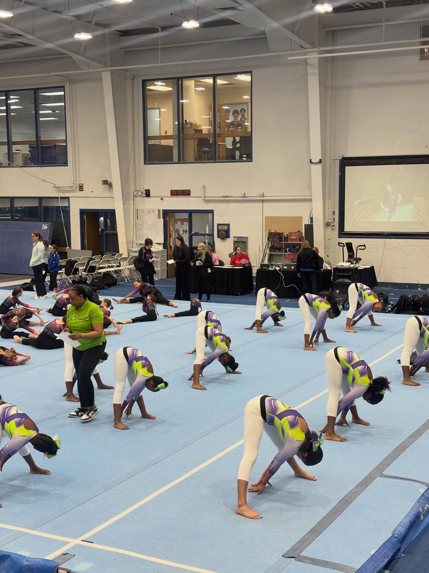 Gymnastics class stretching on blue mats in a large indoor gym.