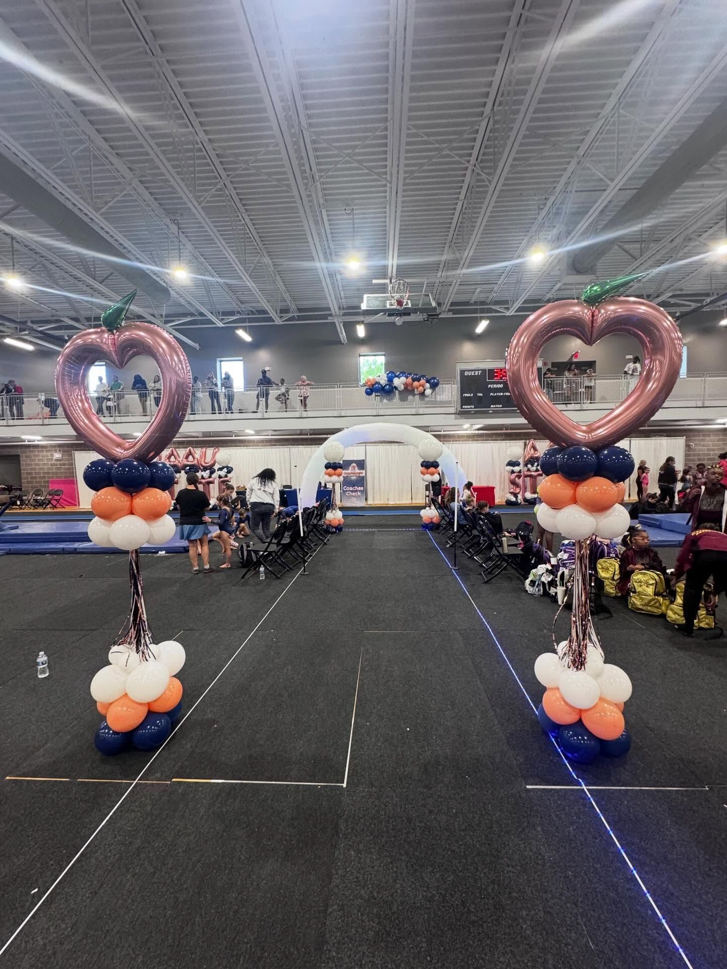 Balloon heart archways framing a decorated event hall with tables and attendees in the background.