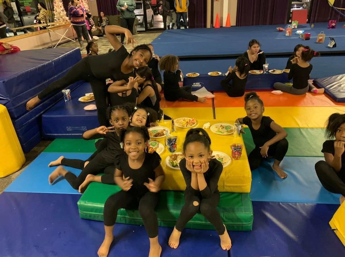 Children doing crafts on mats in a gymnasium, with colorful play equipment and padded floor.