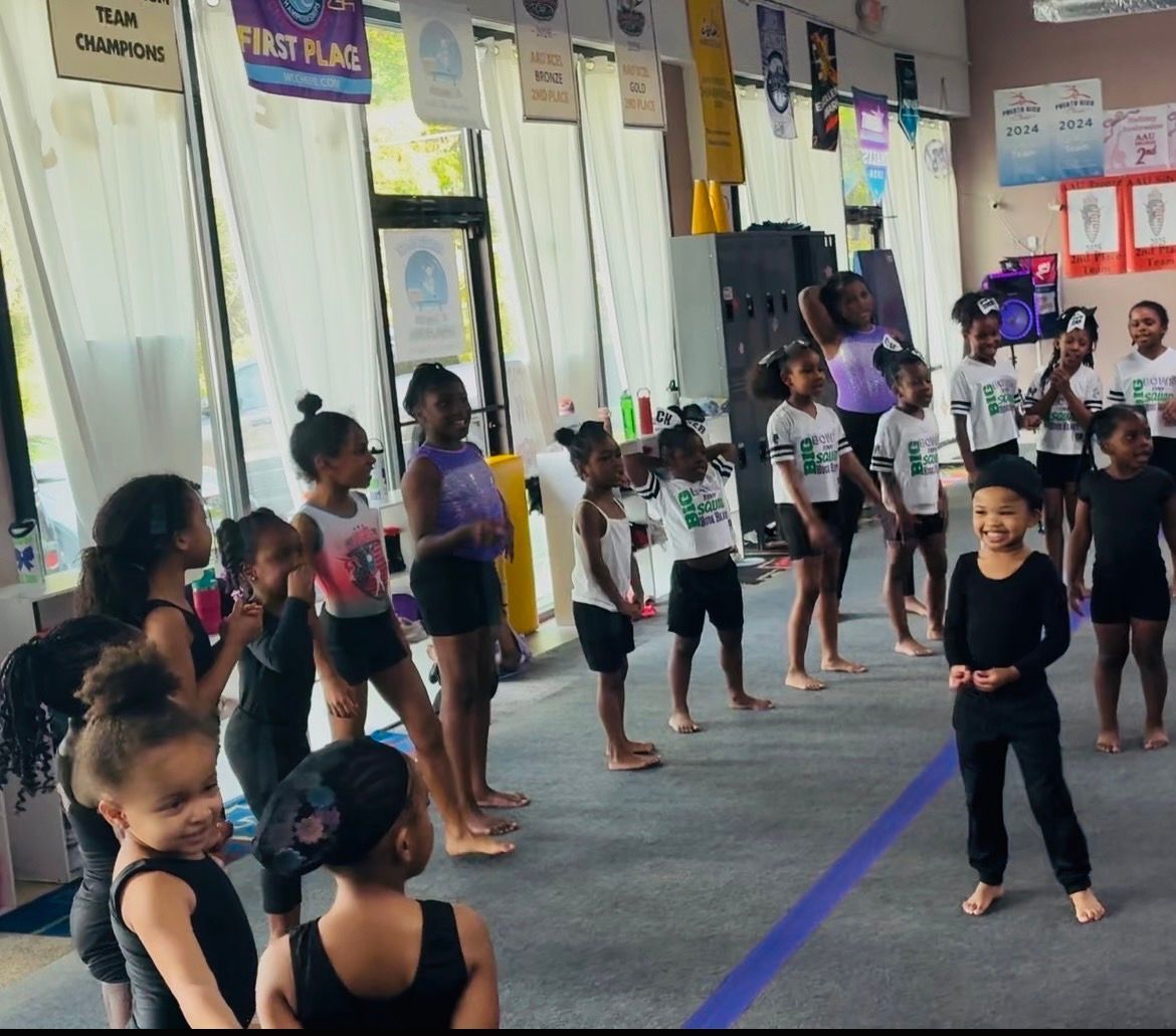 Gymnastics class stretching on blue mats in a large indoor gym.