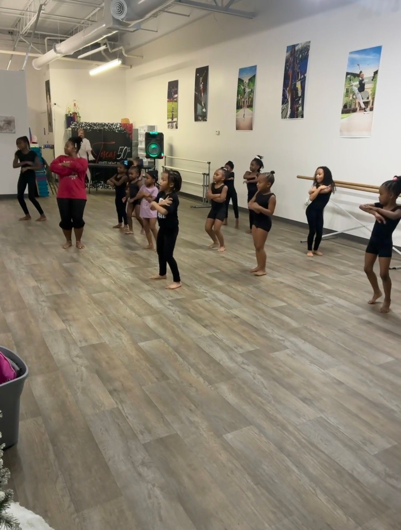 Six dancers in purple, green, and white costumes posing in a studio with a wooden floor