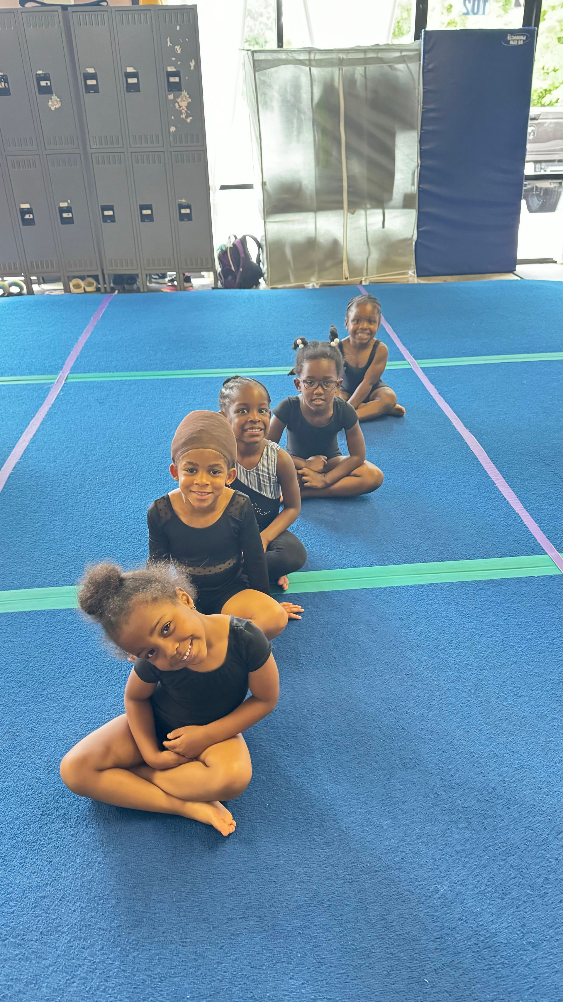 Gymnasts posing on a podium with a sign reading “Angels in the Gym,” holding medals and raising arms.