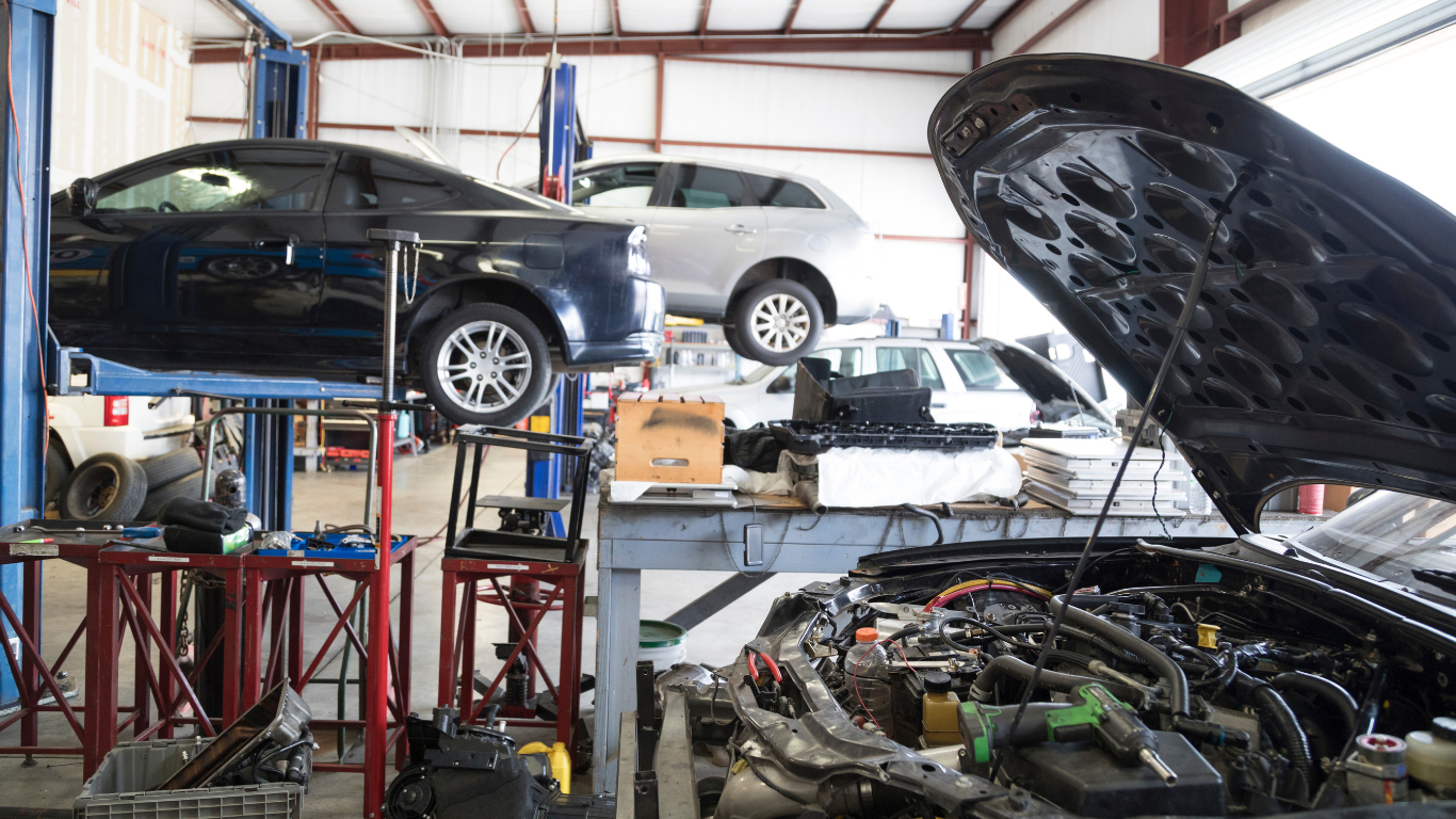 Cars in an auto repair shop, with one lifted on a rack and another with its hood open in the foreground