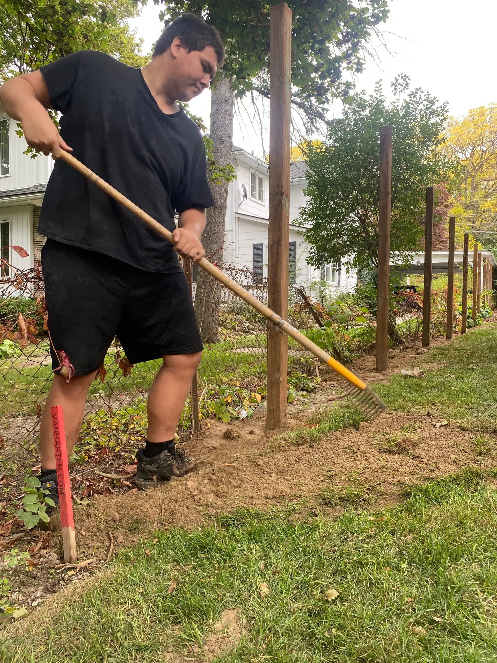 Person raking dirt, preparing a garden bed with wooden posts in a yard.