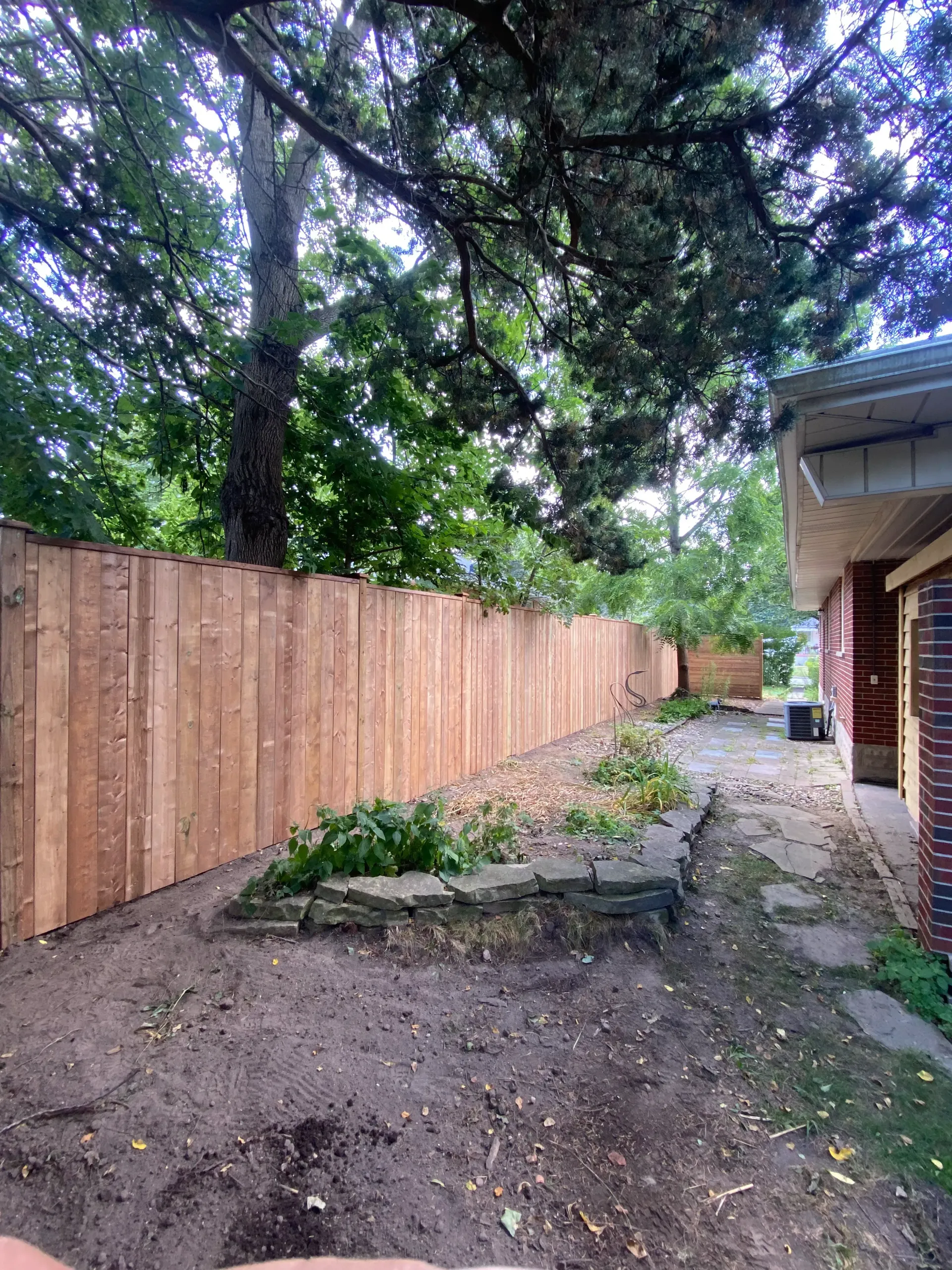 Wooden fence alongside a brick house and yard with trees.