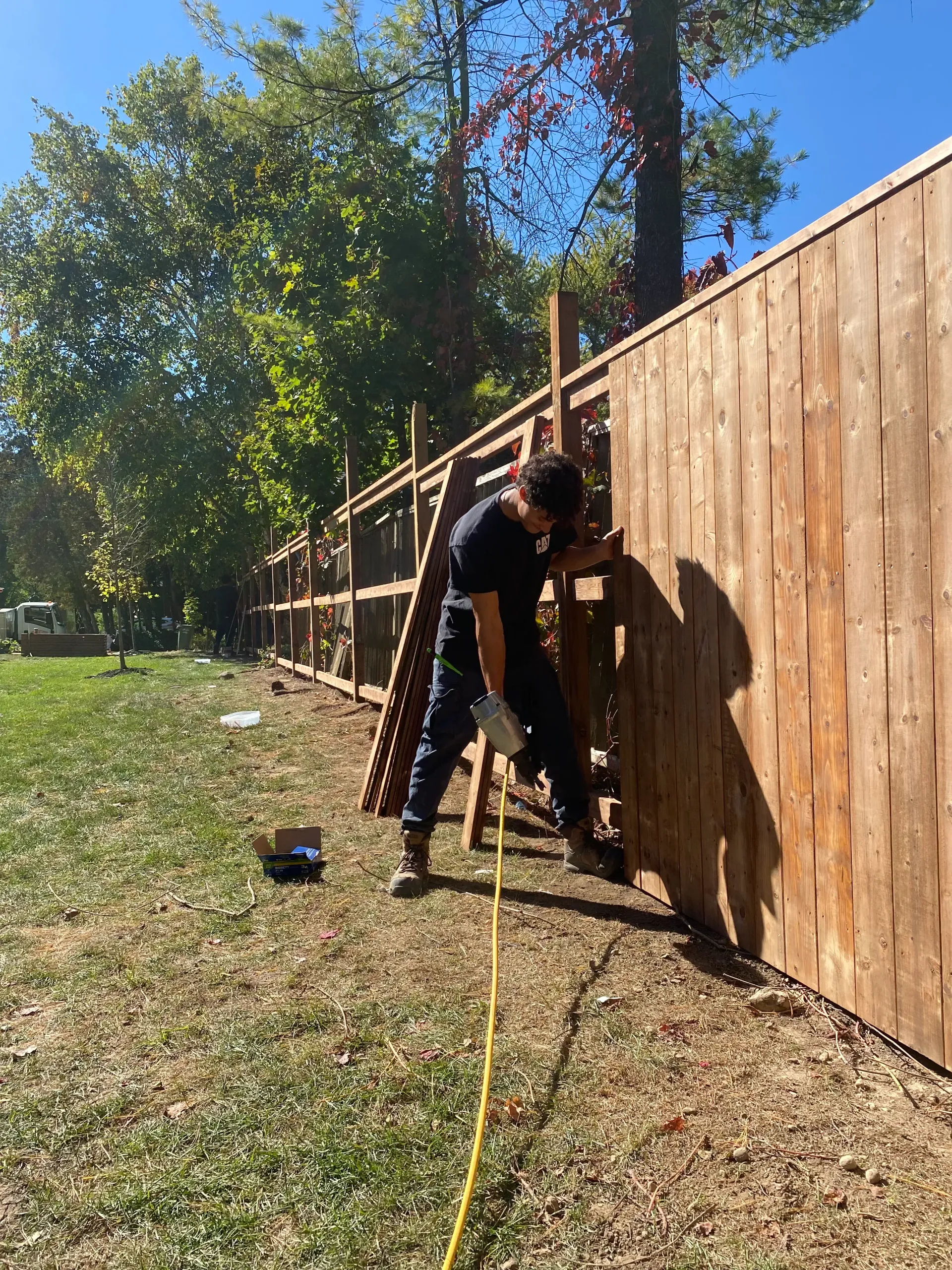 Person working on wooden fence outdoors on a sunny day.
