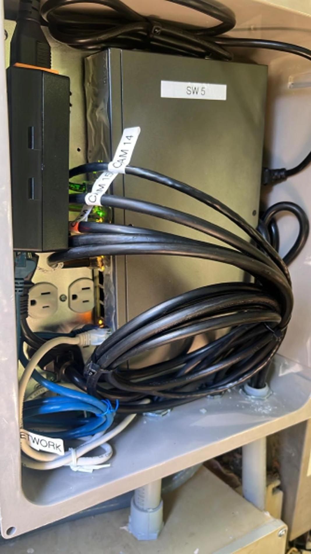 Open metal cabinet with bundled black cables, power strip, and labeled gray box inside.