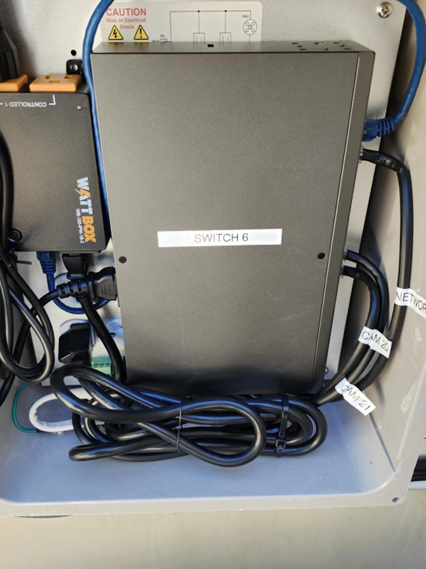 Gray network switch in a cabinet with bundled cables and a label reading “SWITCH 6”