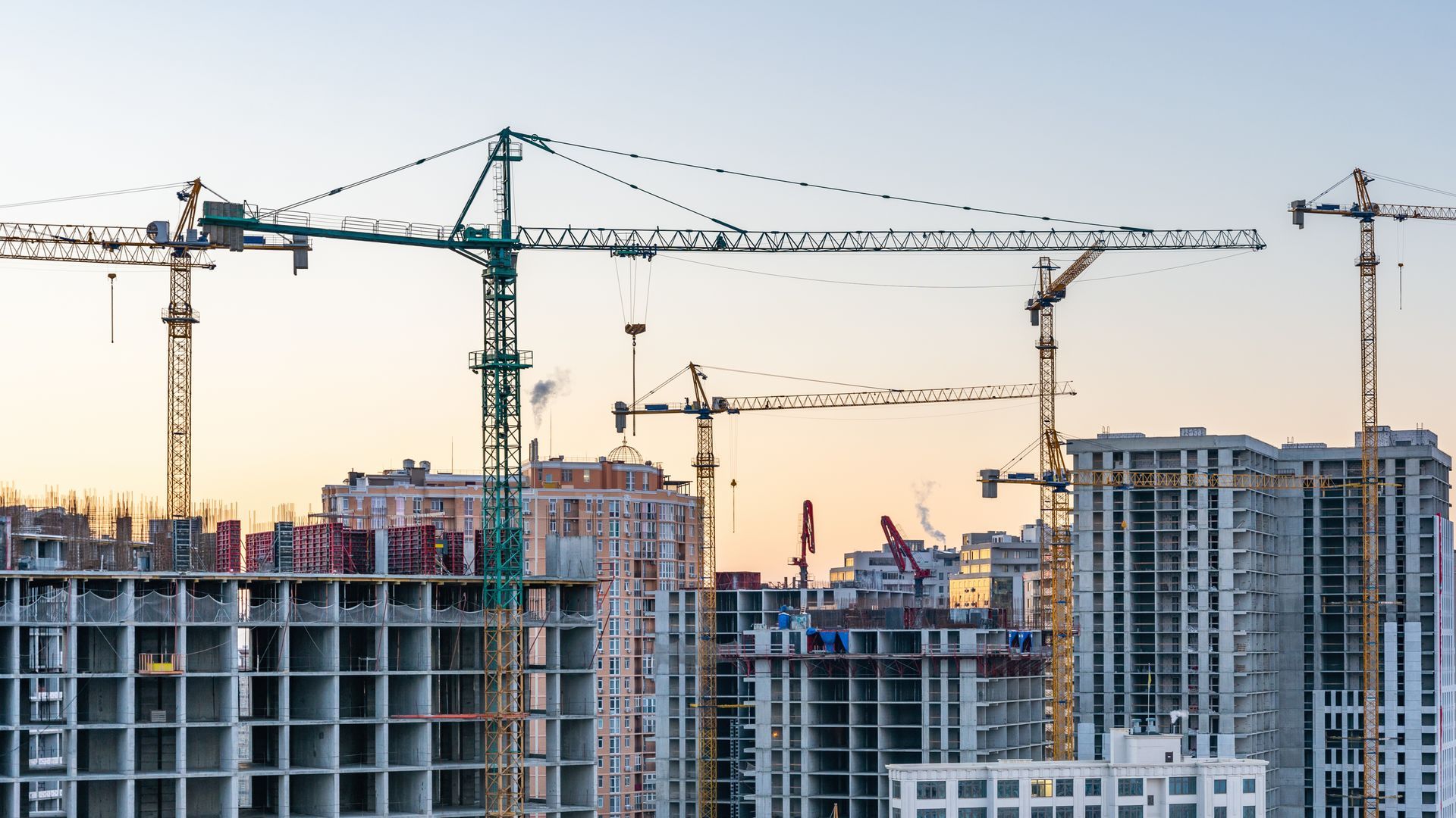 Construction site with high-rise buildings and several cranes at sunset
