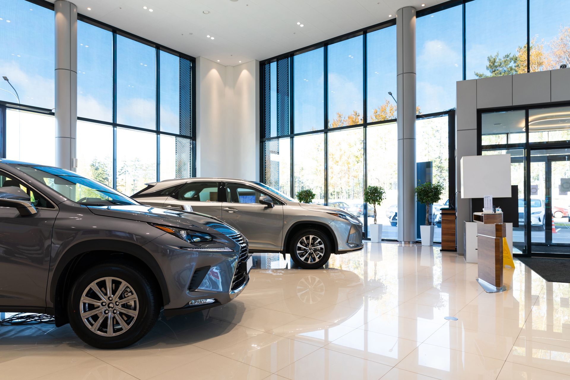 Bright car showroom with two cars, glossy floors, and large windows overlooking city buildings