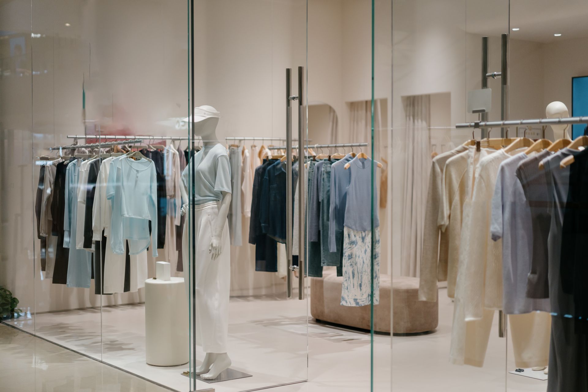 Bright clothing store interior with racks of pastel and neutral garments behind glass walls