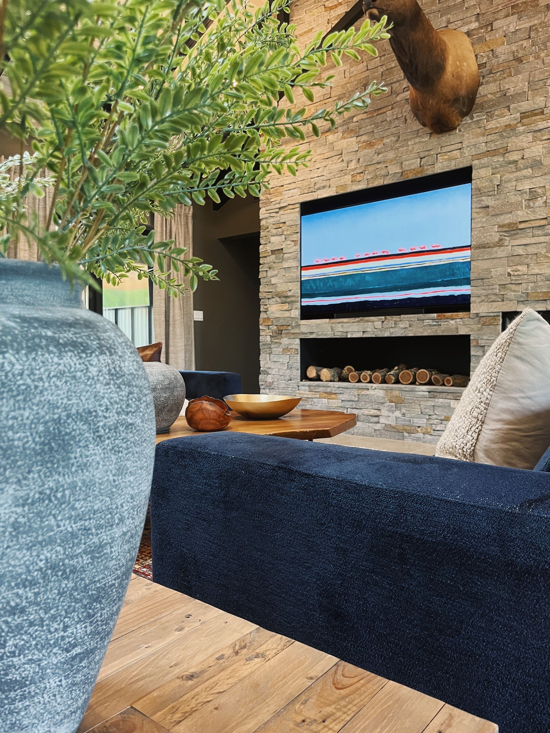Cozy living room with fireplace, wall TV showing a seascape, and a large blue chair in the foreground
