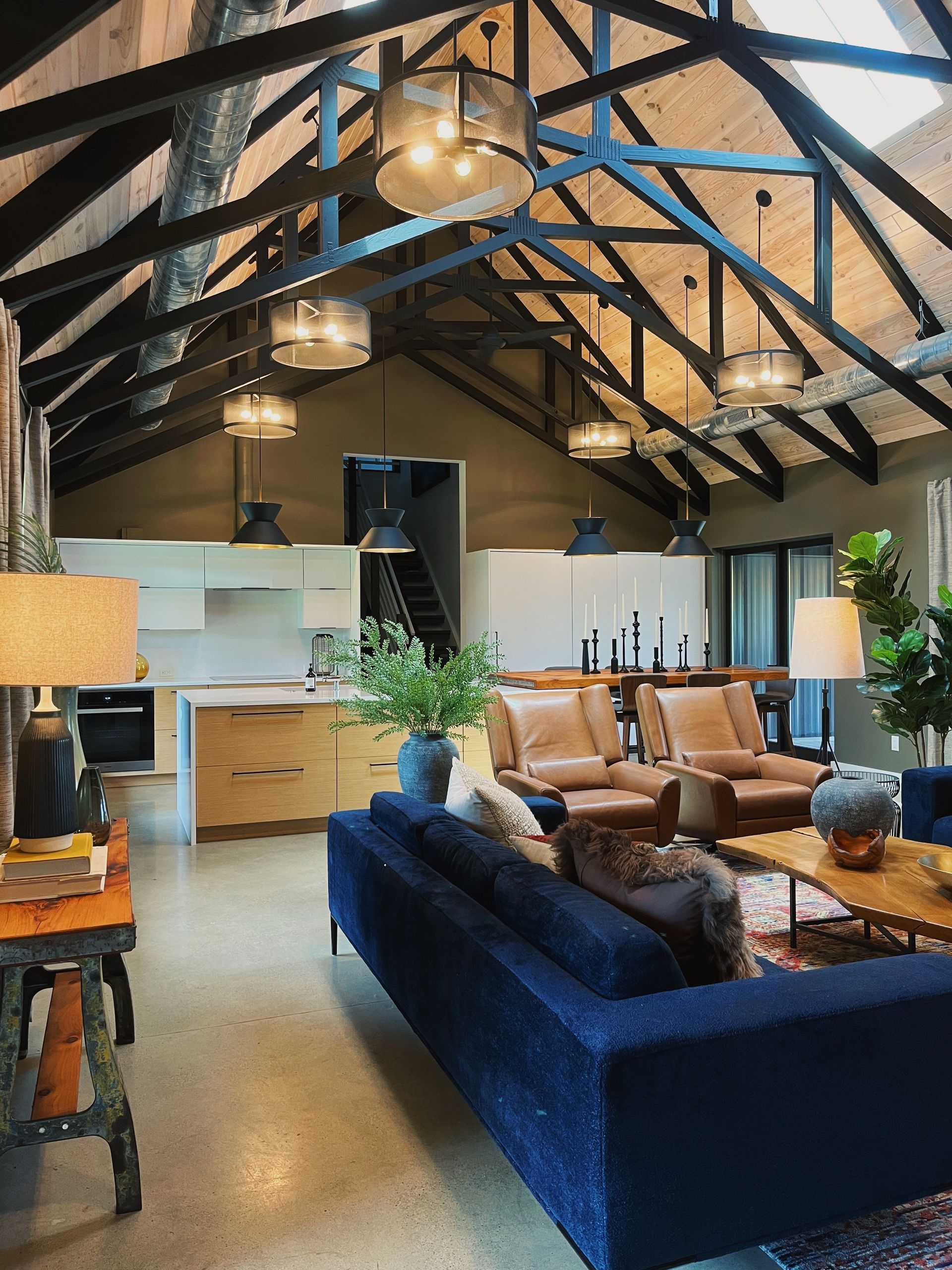 Loft living room with exposed beams, blue sofa, tan chairs, and hanging pendant lights