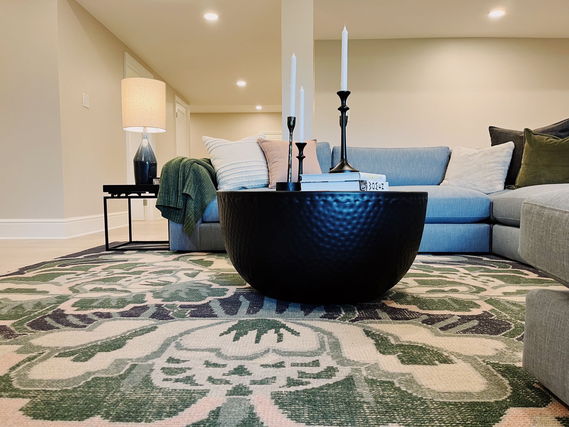 Modern living room with blue sofa, patterned rug, and black coffee table with candles