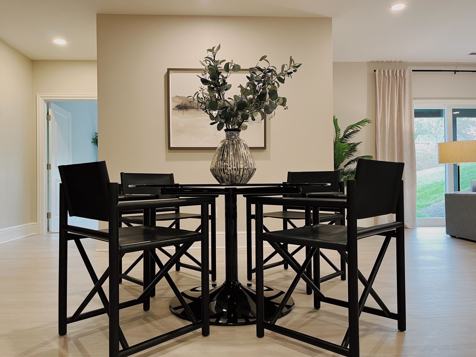 Black dining table with four chairs and a vase centerpiece in a bright modern room