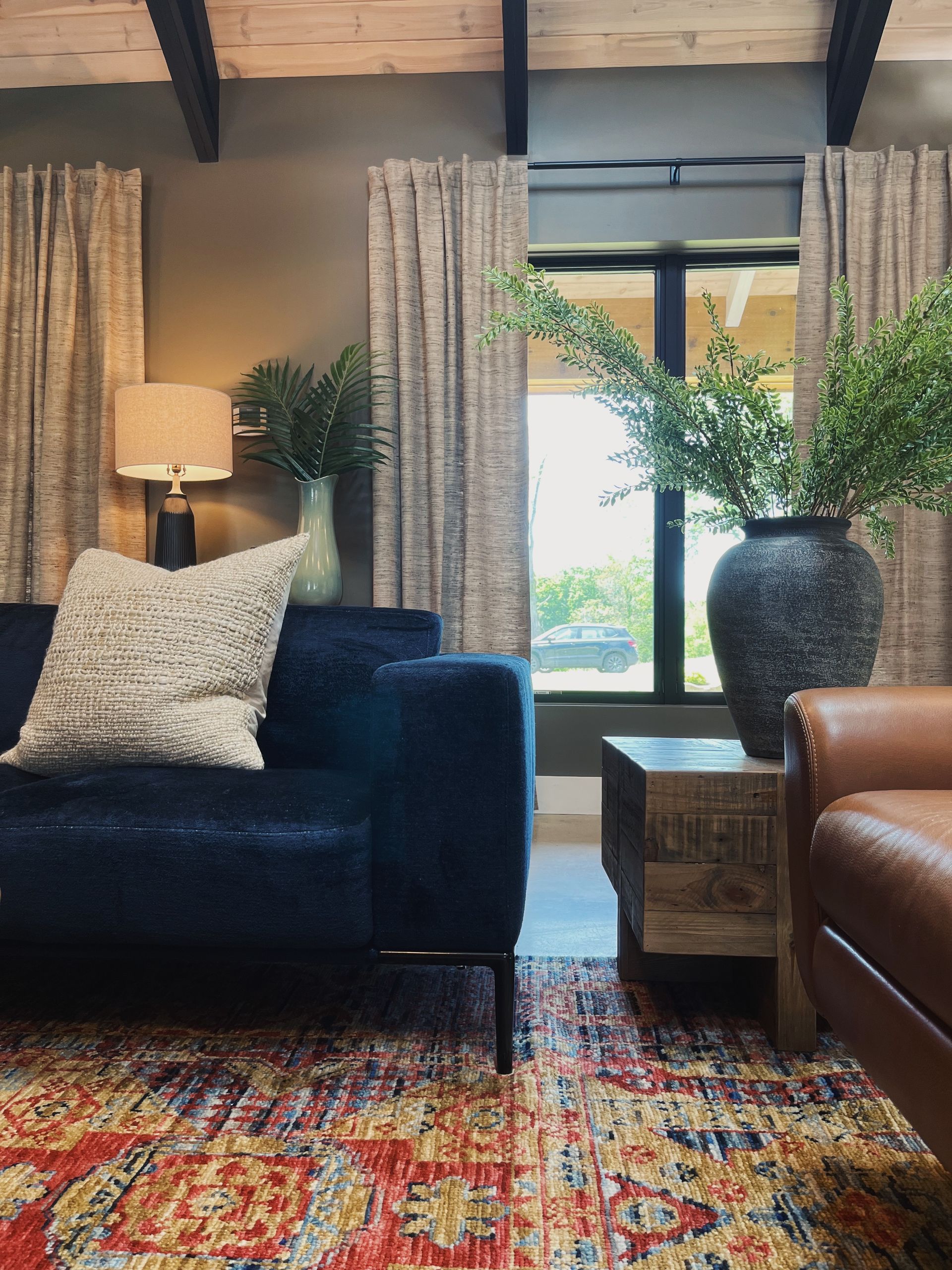 Cozy living room with dark blue sofa, leather chair, patterned rug, and tall windows with curtains.