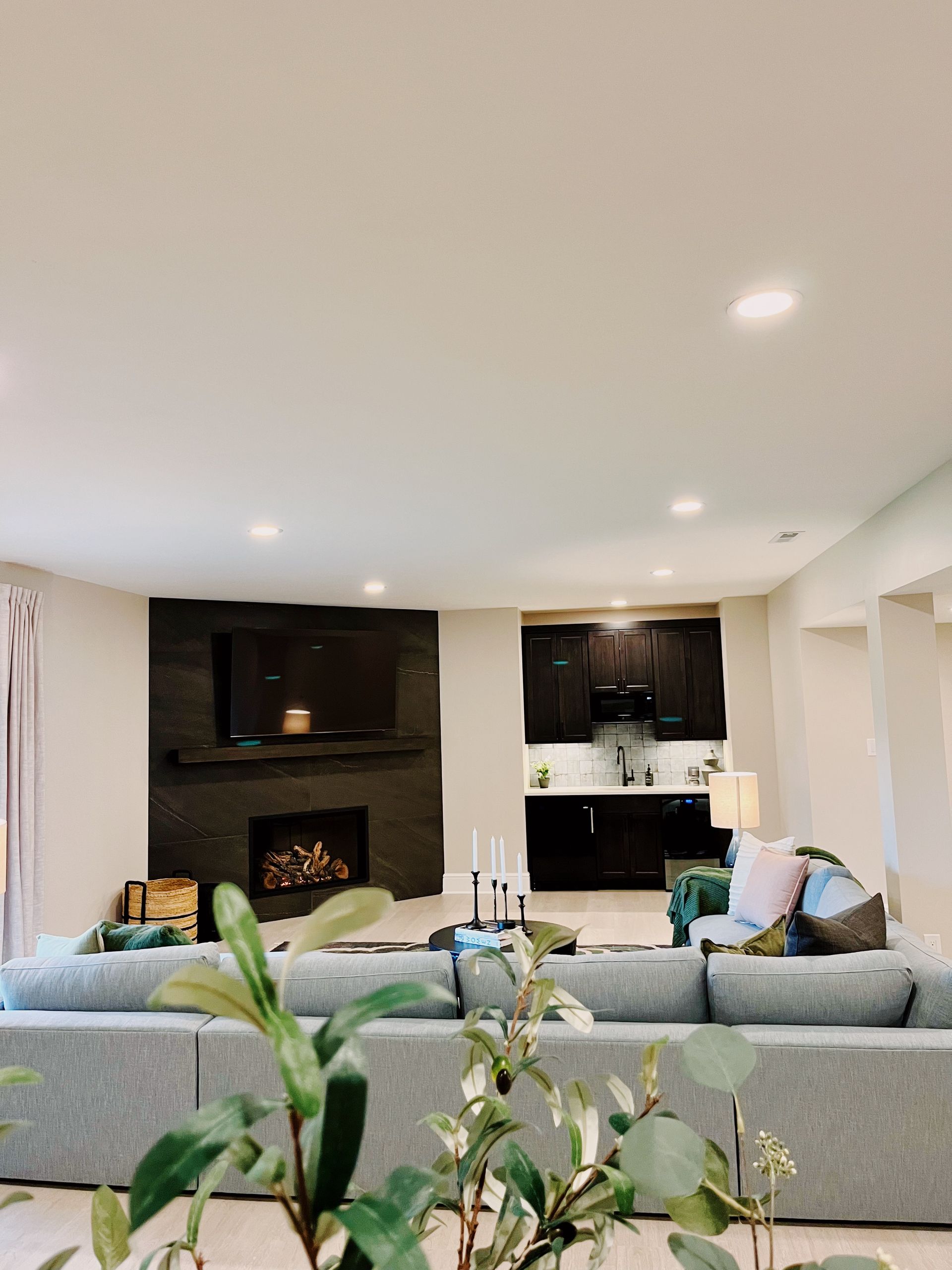 Modern living room with gray sofas, dark fireplace, and kitchen island in the background