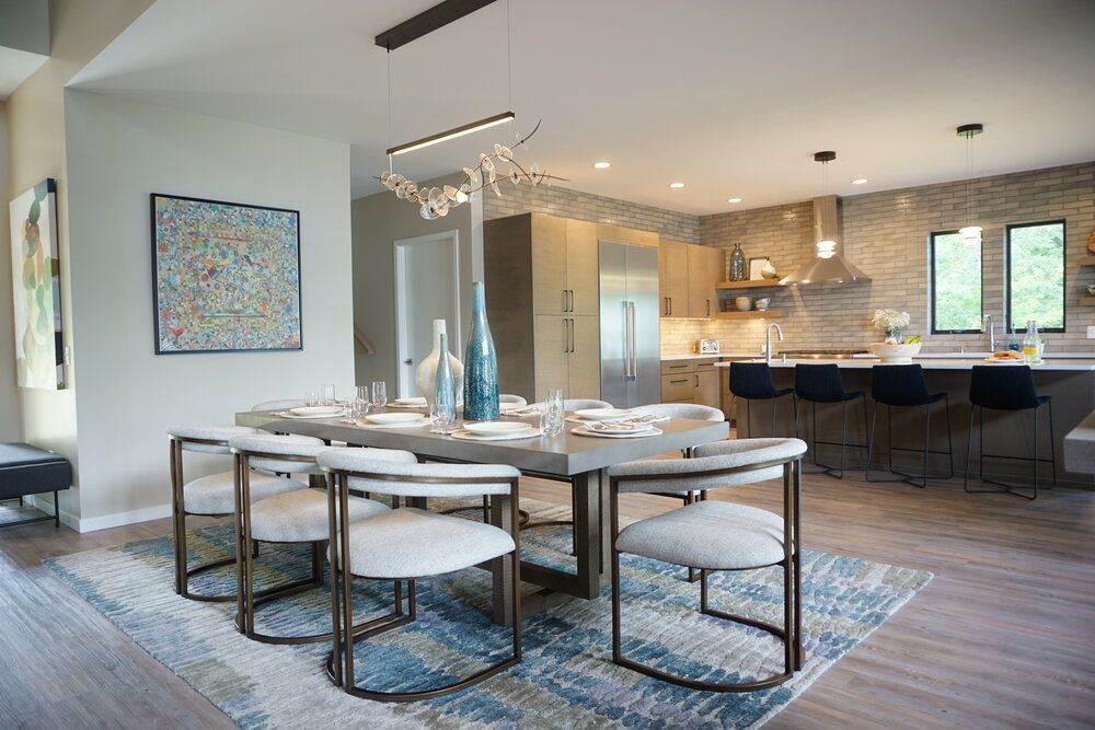 Modern open-plan dining and kitchen area with a table, stools, blue rug, and bar seating