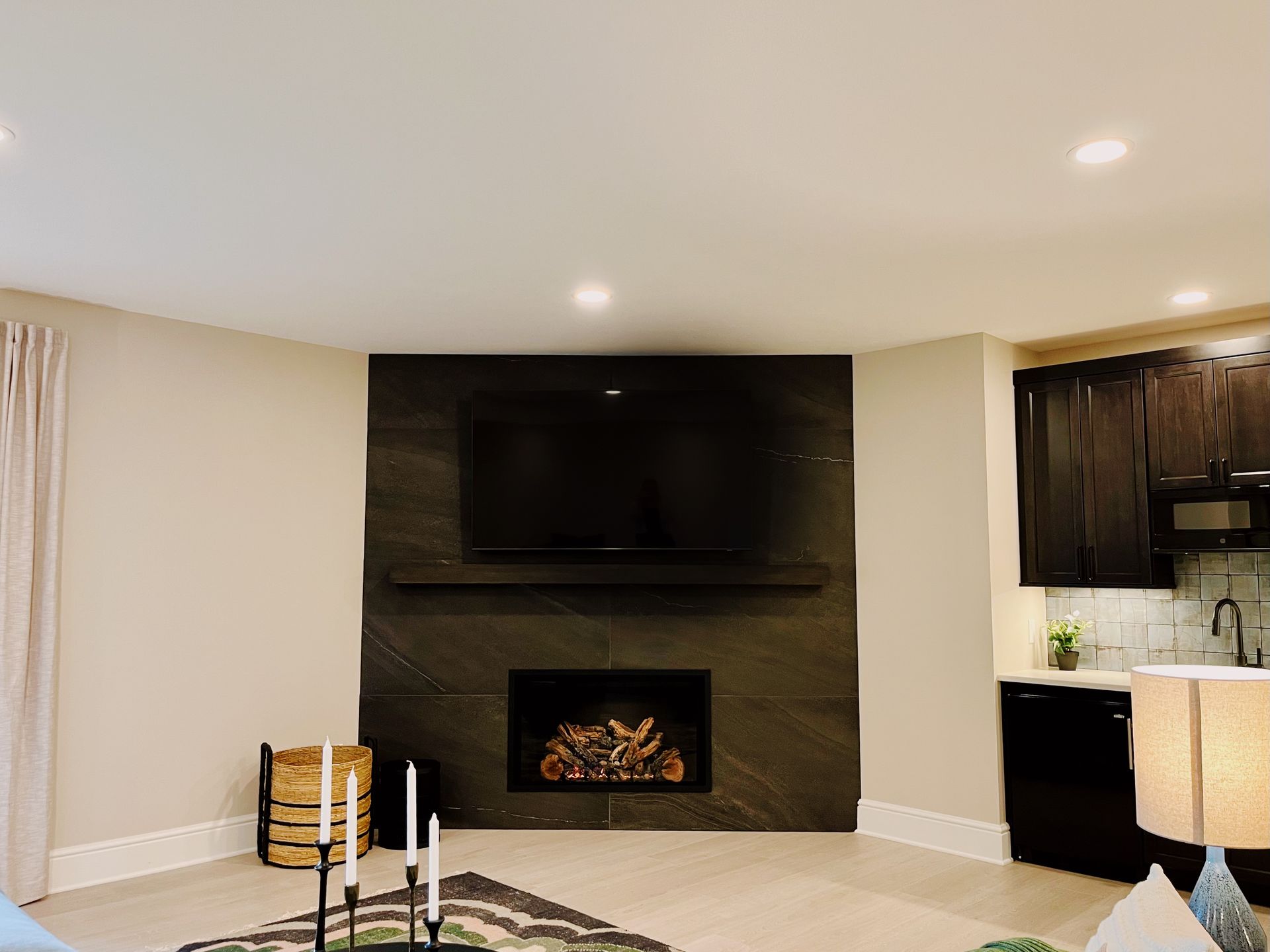 Modern living room with black fireplace, wall-mounted TV, and adjoining kitchen area.