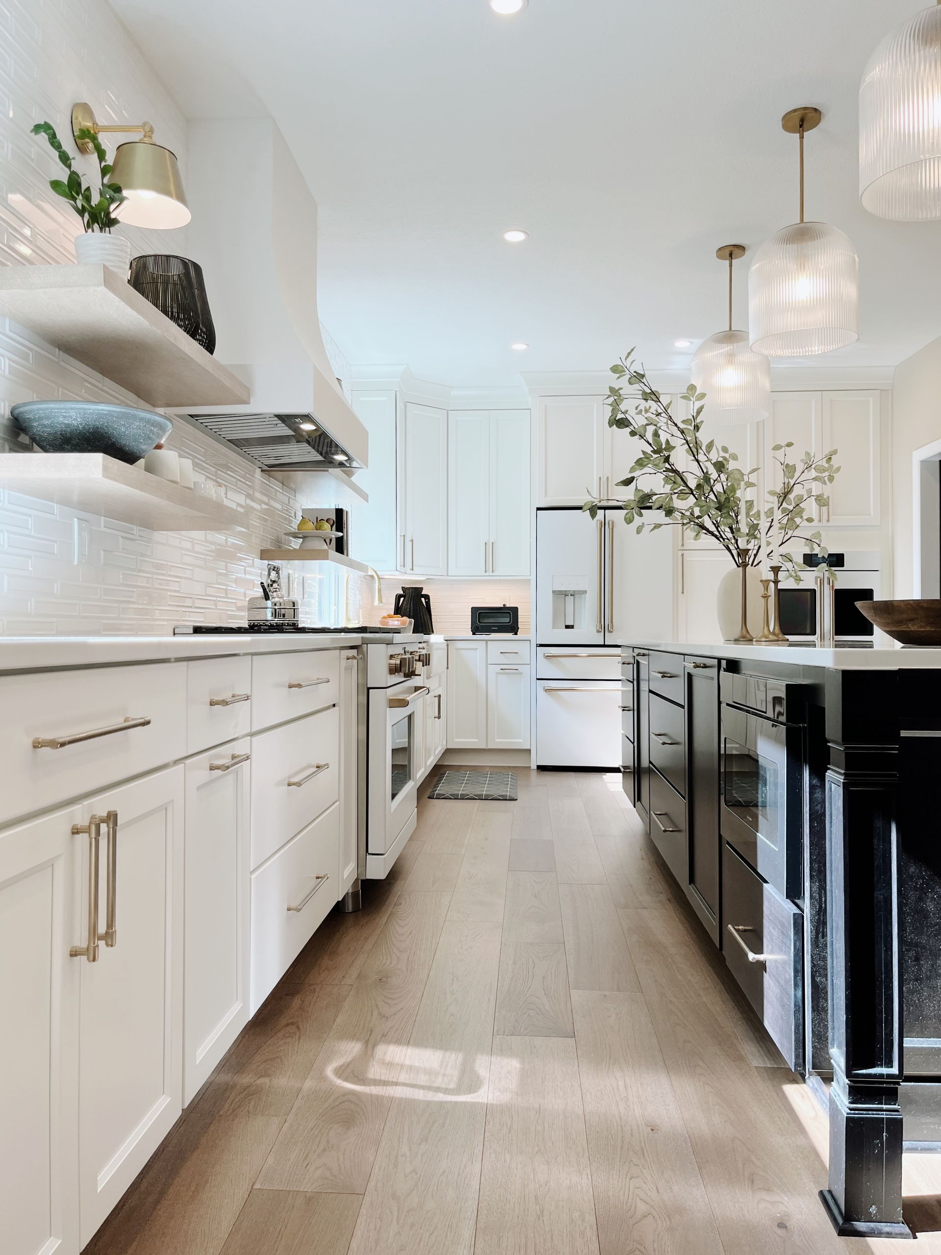 Bright white modern kitchen with black island cabinets, open shelves, and pendant lights