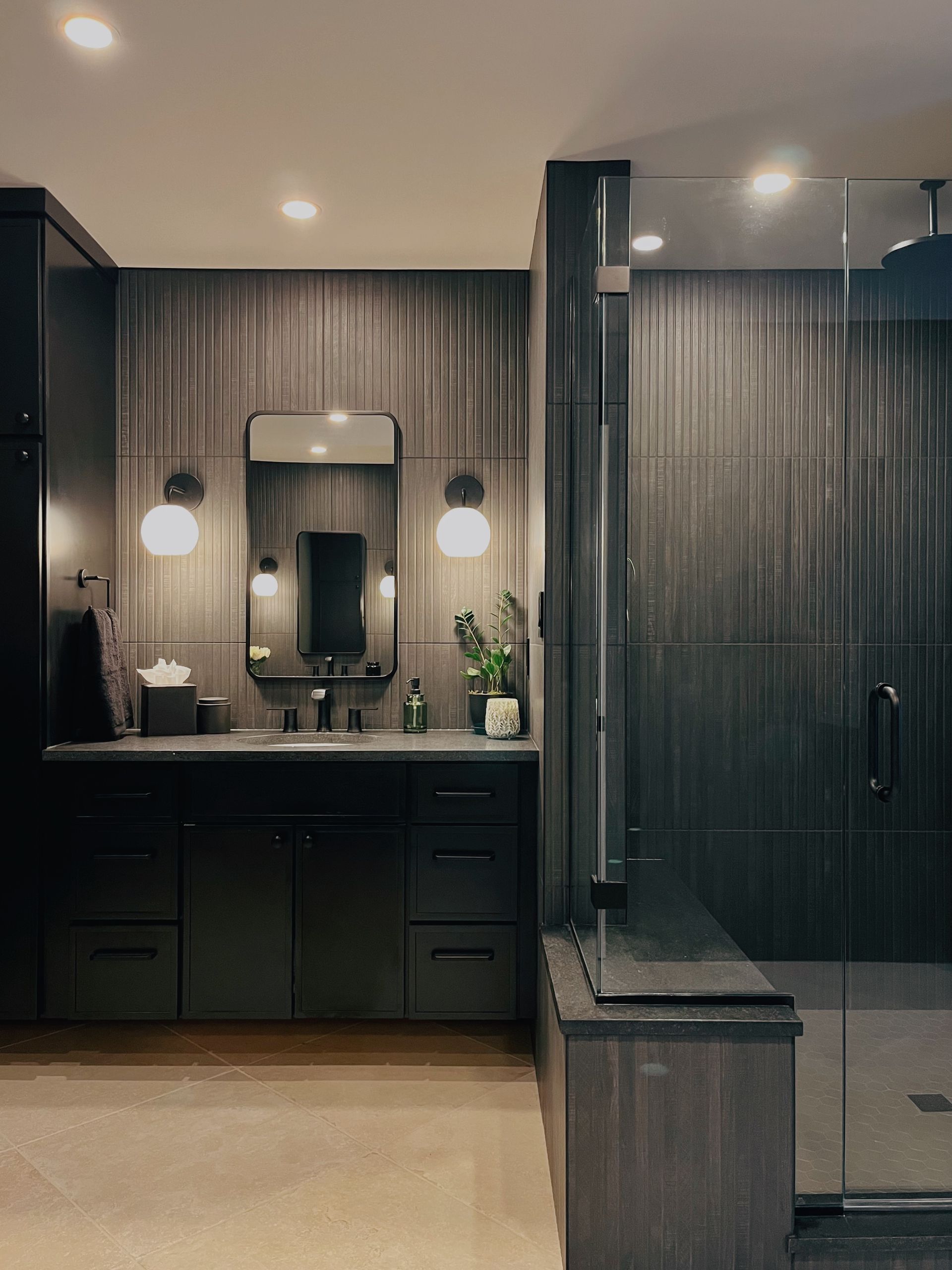 Modern dark bathroom with double vanity, round mirrors, and a glass-enclosed shower.