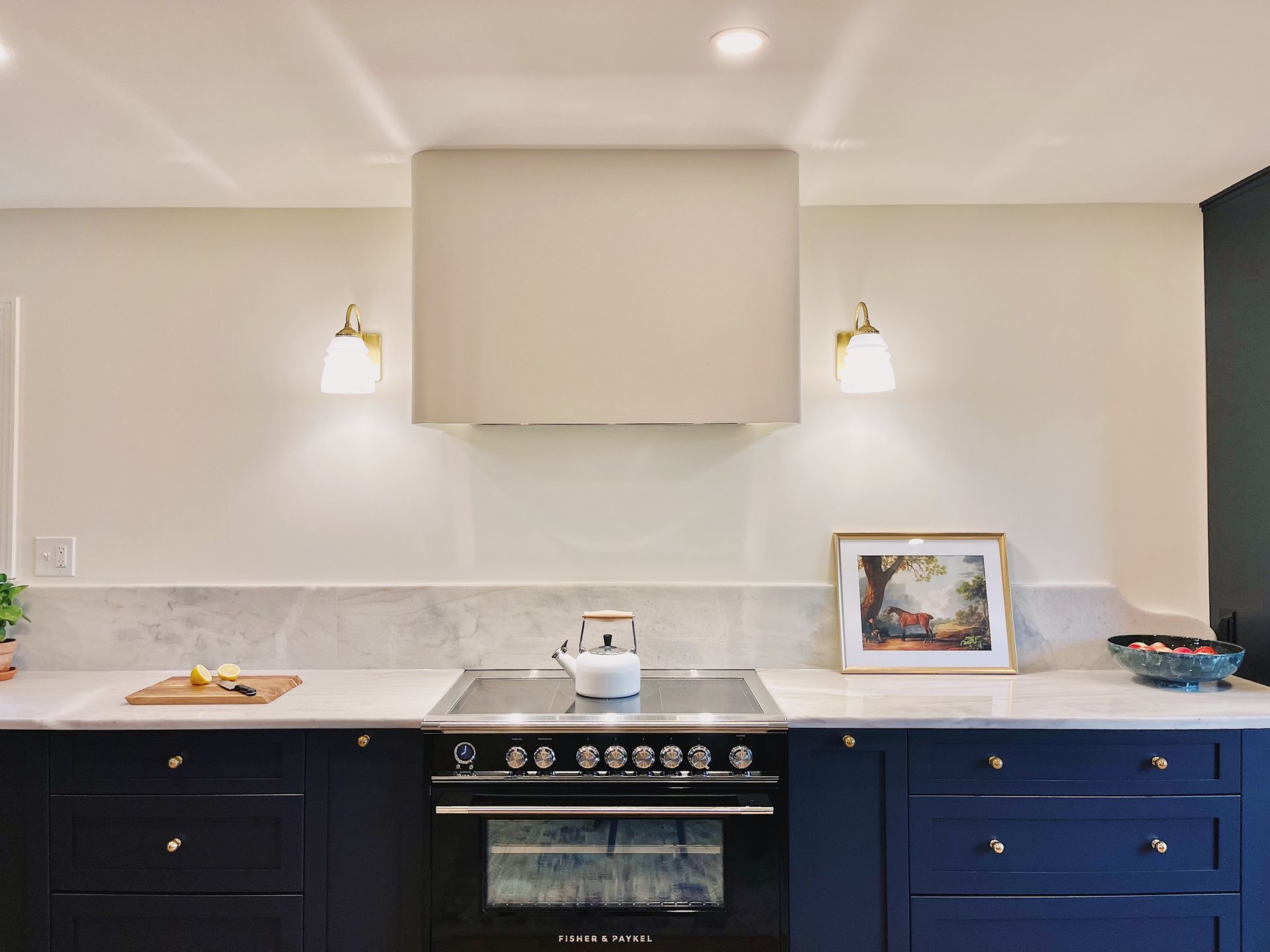 Modern kitchen with navy cabinets, white countertops, stove, and framed art on the counter