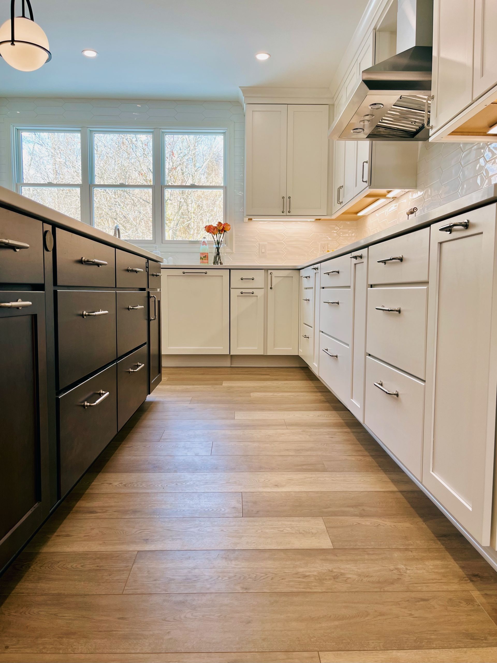 Bright white kitchen with black island, wood floor, and large window above the sink