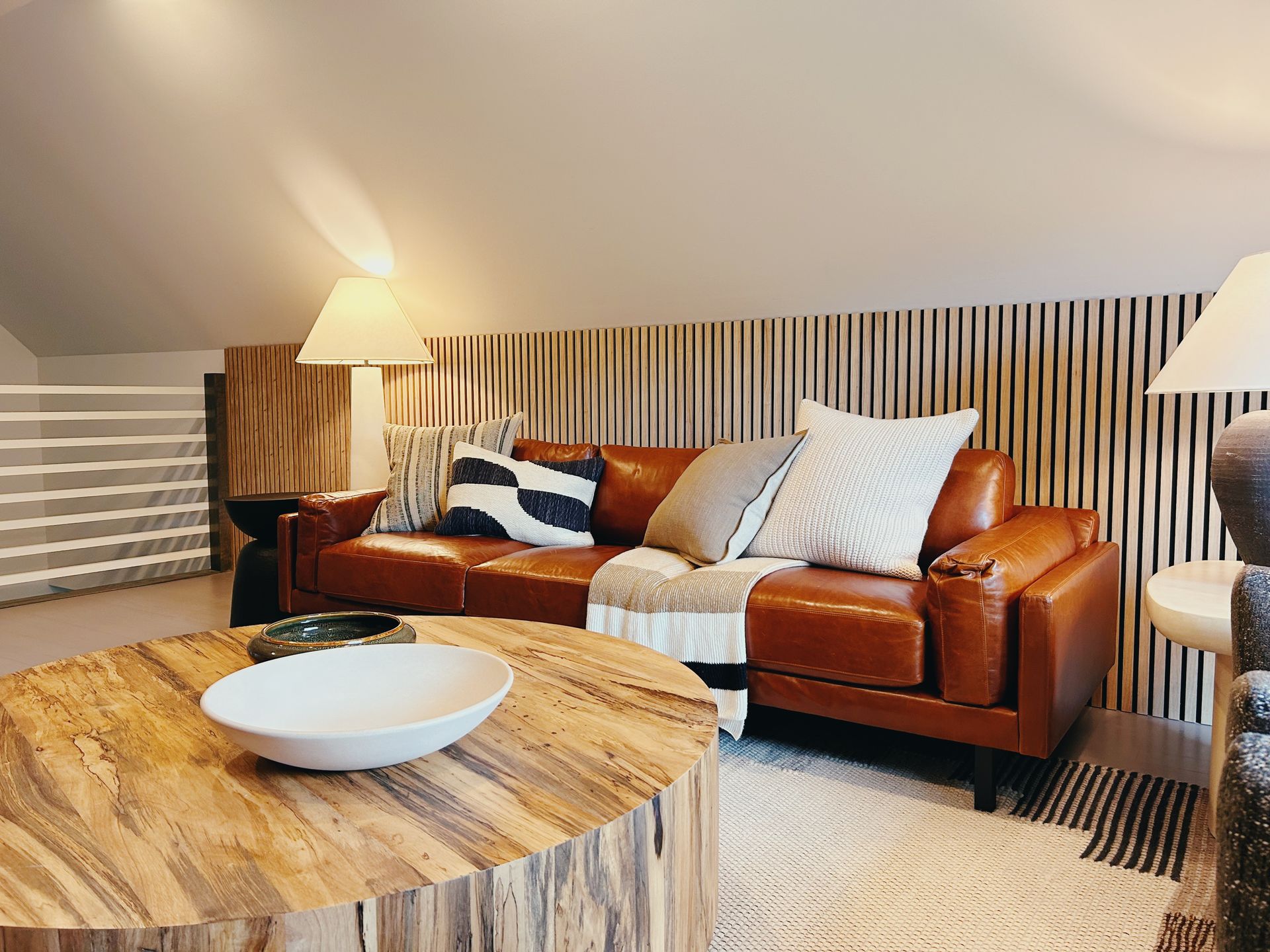 Modern living room with brown leather sofa, round wood coffee table, lamp, and striped accent wall