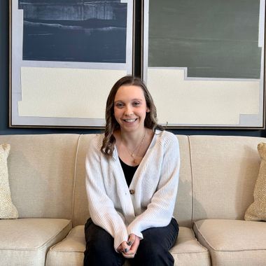 Smiling woman seated on a beige couch in front of abstract wall art