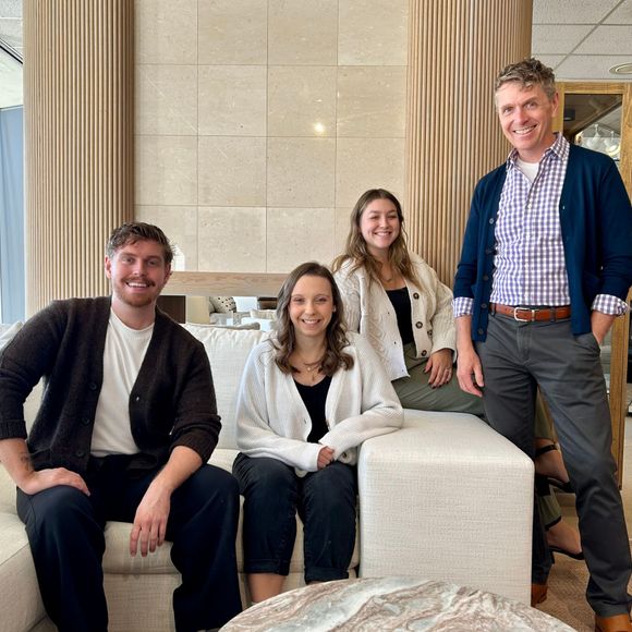 Four people smiling and posing on white lounge chairs in a bright, modern lobby