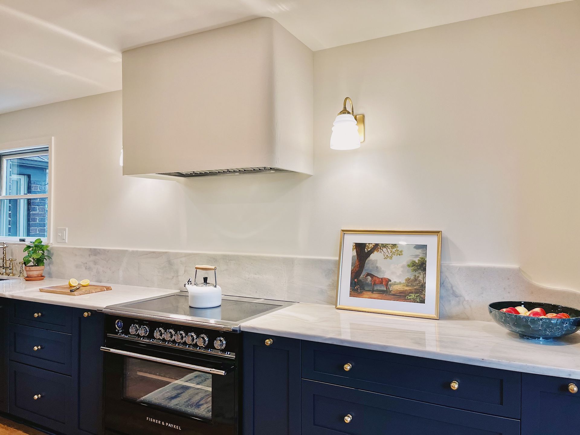 Modern kitchen with navy cabinets, white counters, stove, and decorative bowl and framed art on the counter