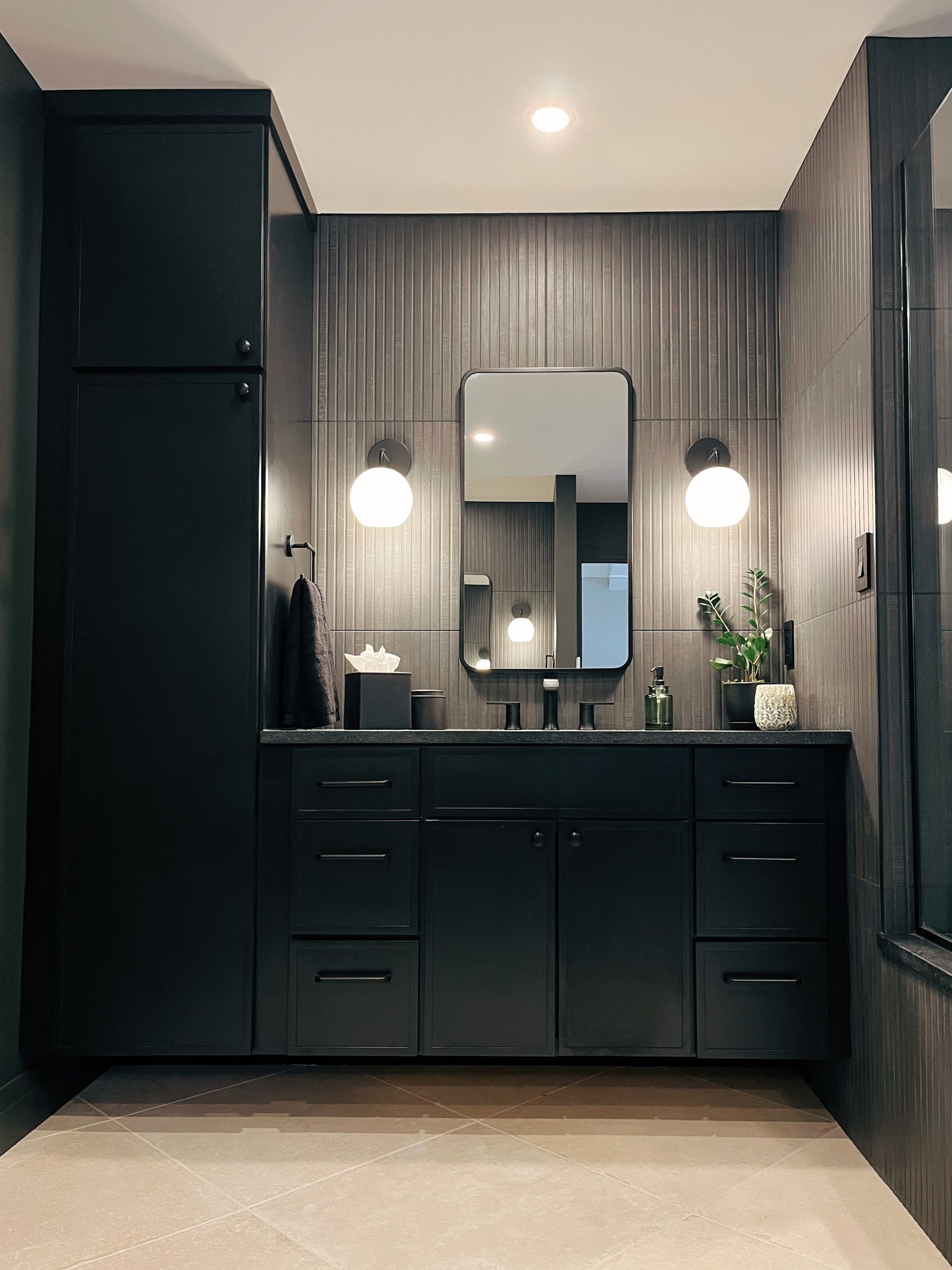 Dark modern bathroom vanity with mirror, black cabinets, and two lit wall sconces