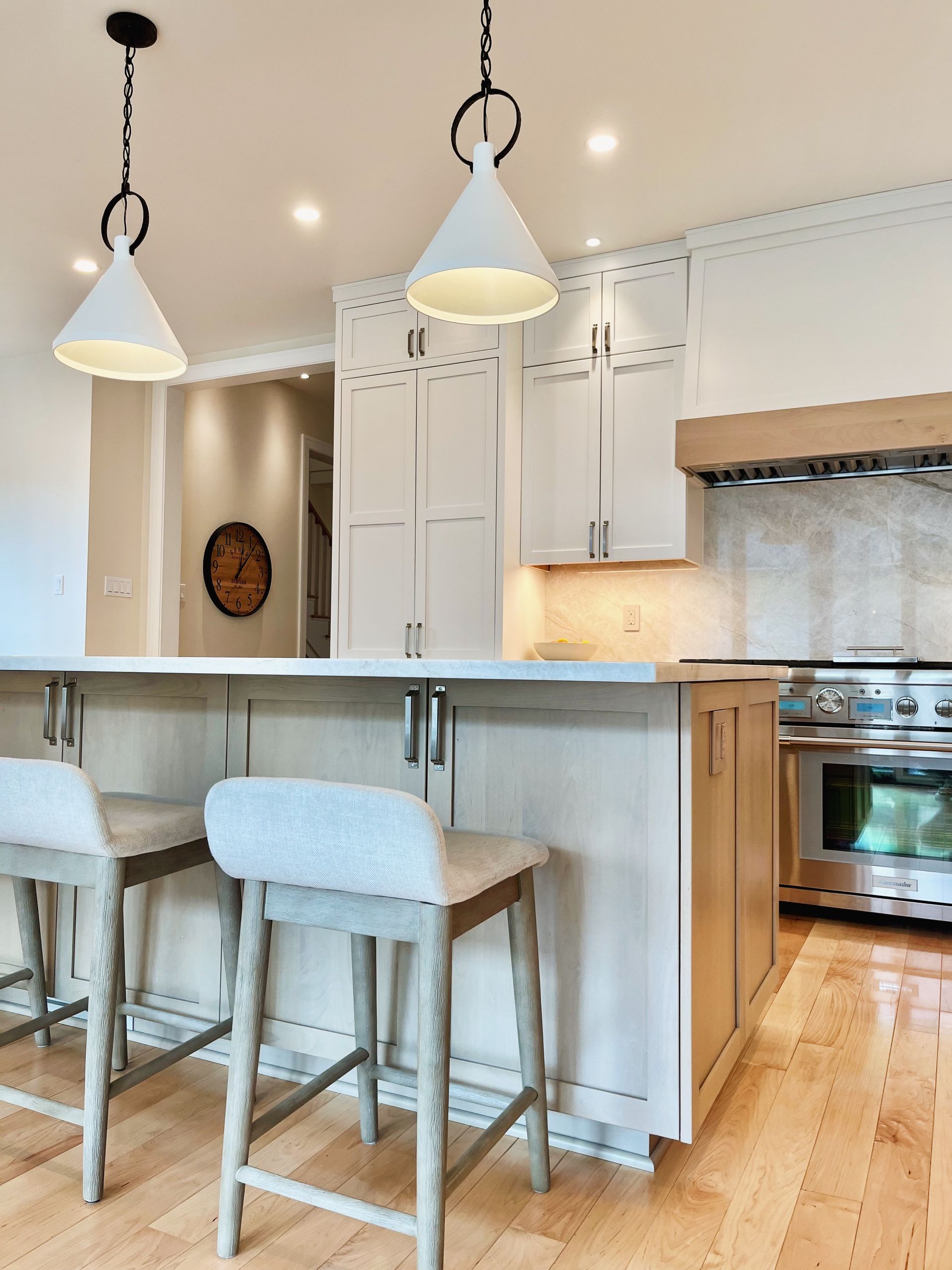 Bright kitchen with white cabinets, island stools, pendant lights, and hardwood floors