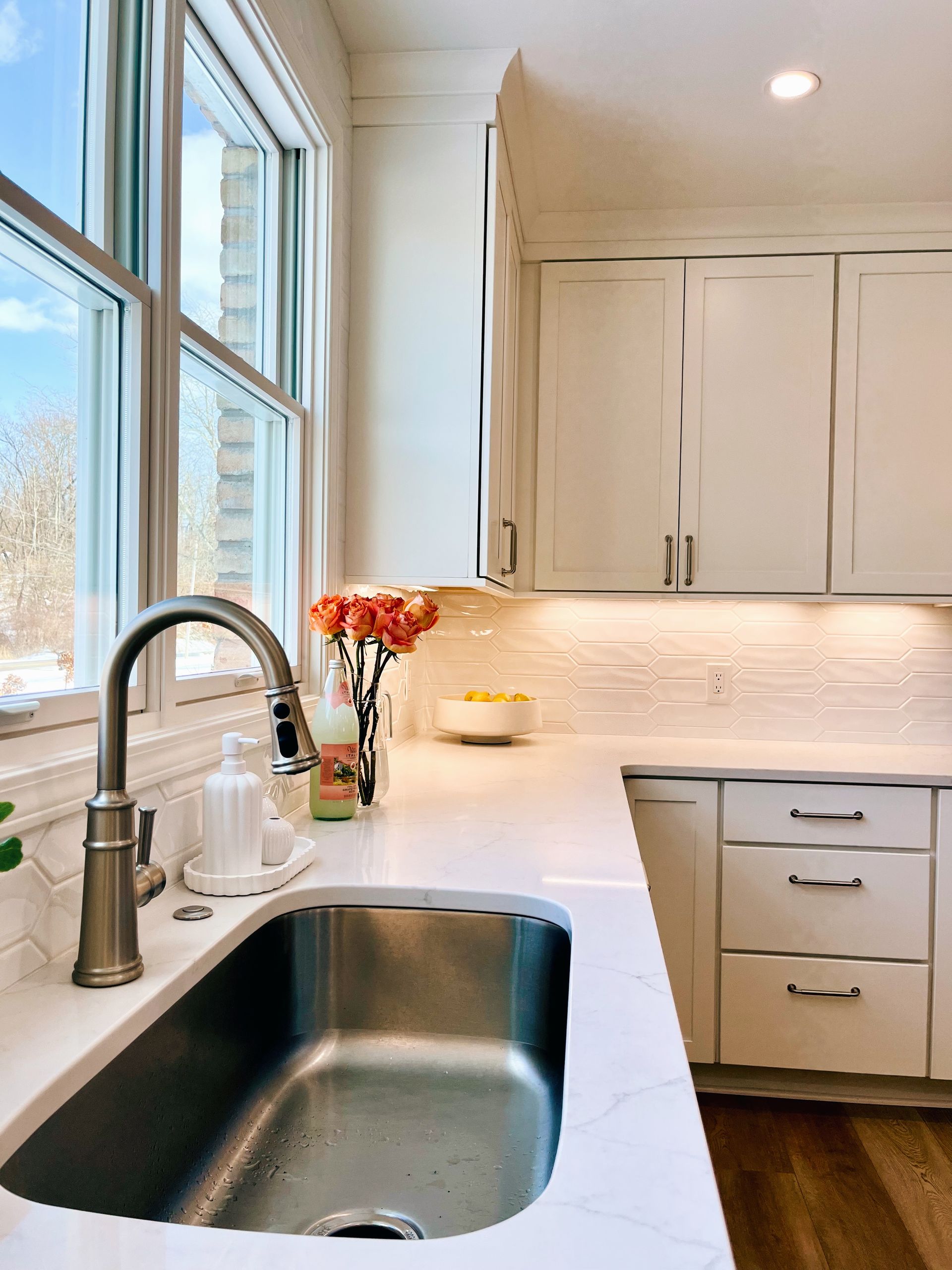 Bright modern kitchen with white cabinets, stainless sink, and window over the counter