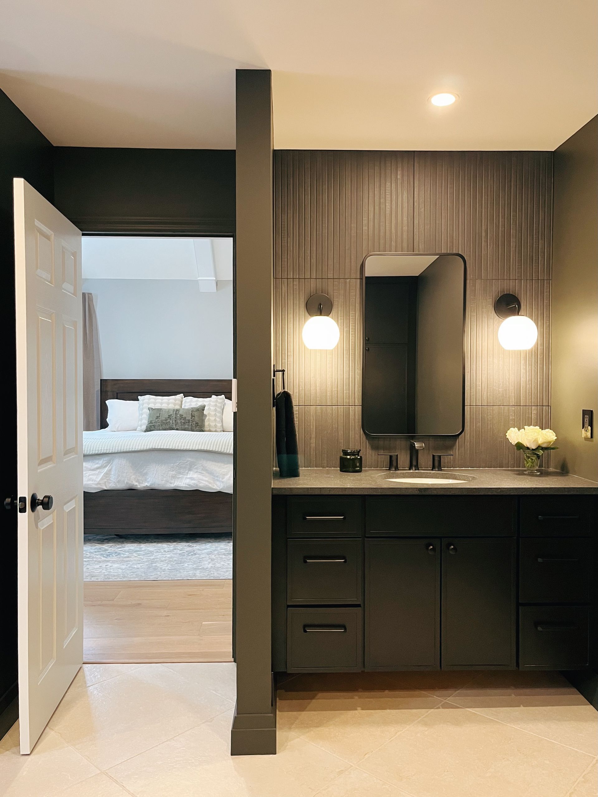 Bedroom vanity area with black cabinets, mirror, wall sconces, and open door to a bed.
