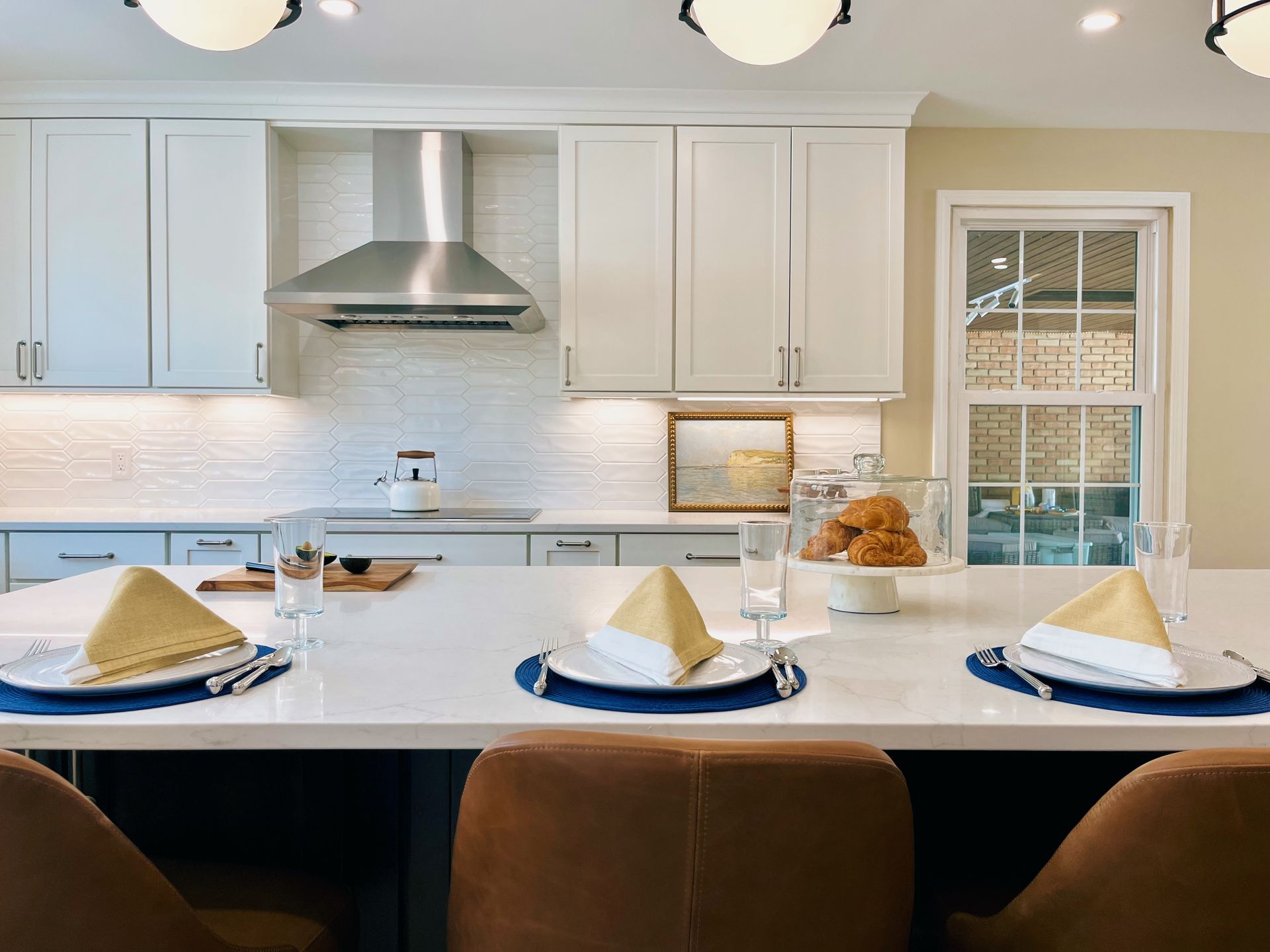 Modern kitchen with white cabinets, blue chairs, and a large island set with folded napkins and plates