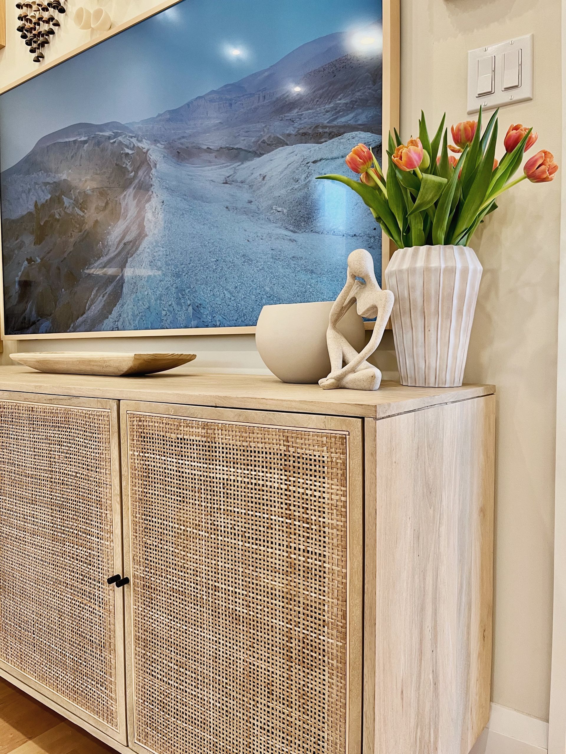 Wicker cabinet with ceramic vases, tulips, and a coastal wall print in a bright room