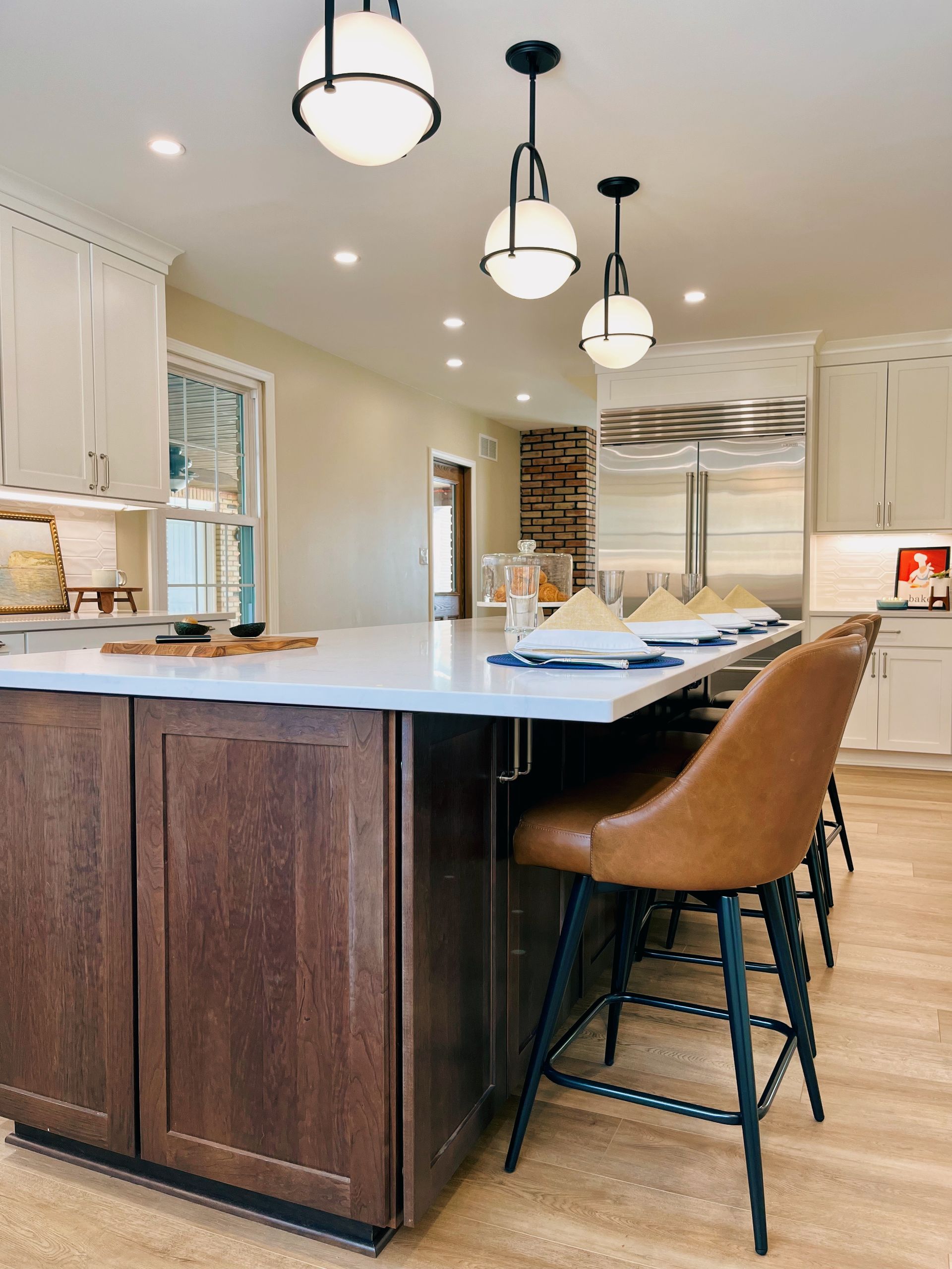 Modern kitchen with large island, pendant lights, brown stools, and white cabinetry