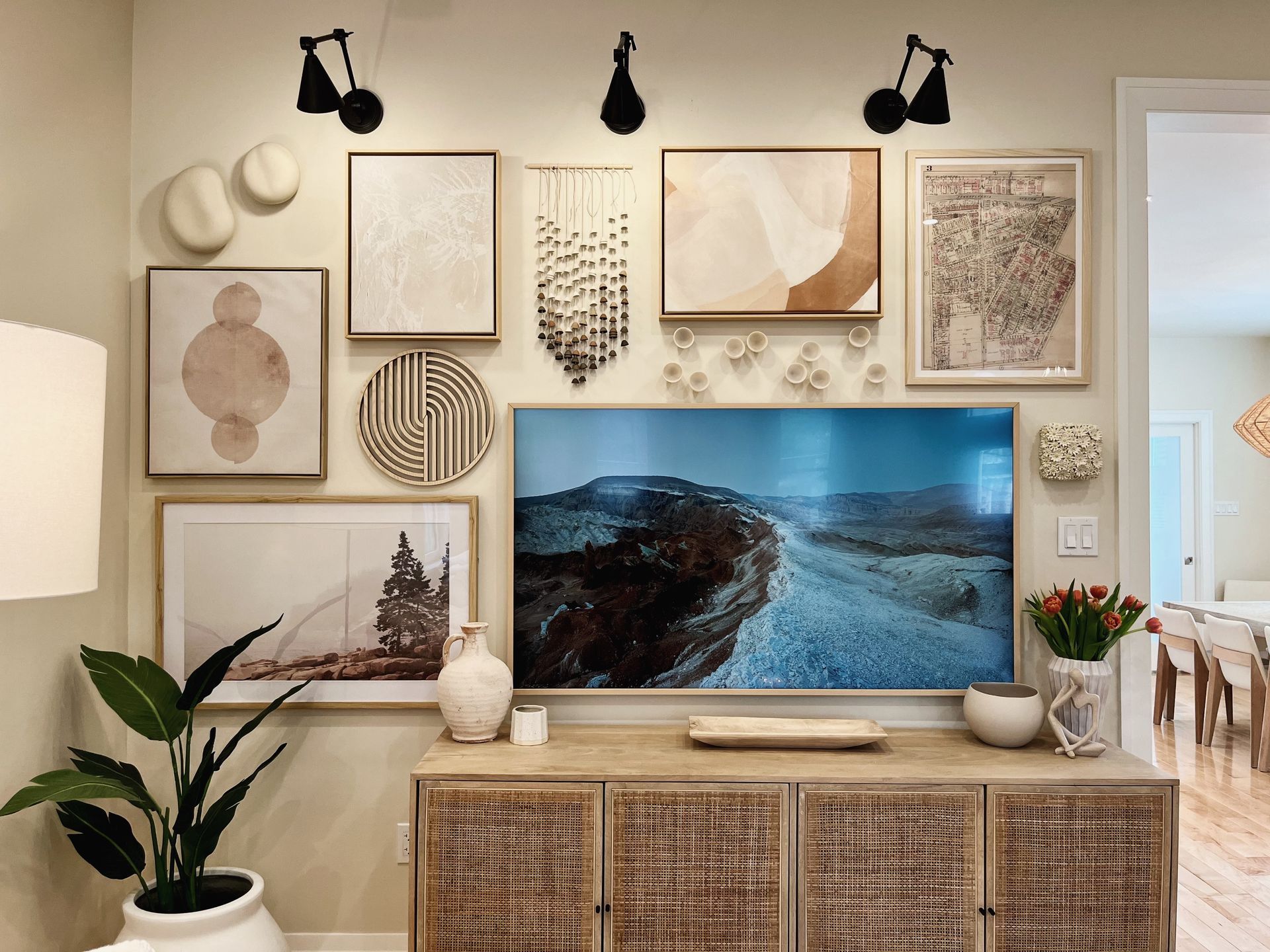 Cozy living room wall with framed art, sconces, and a TV above a wooden cabinet and plants