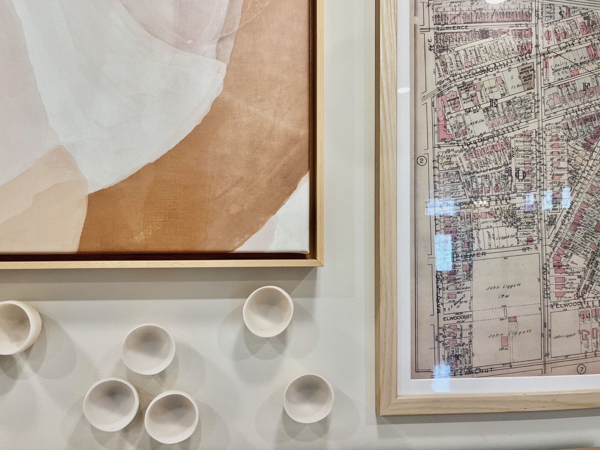Framed abstract art and a framed map hang above white ceramic cups on a wall.