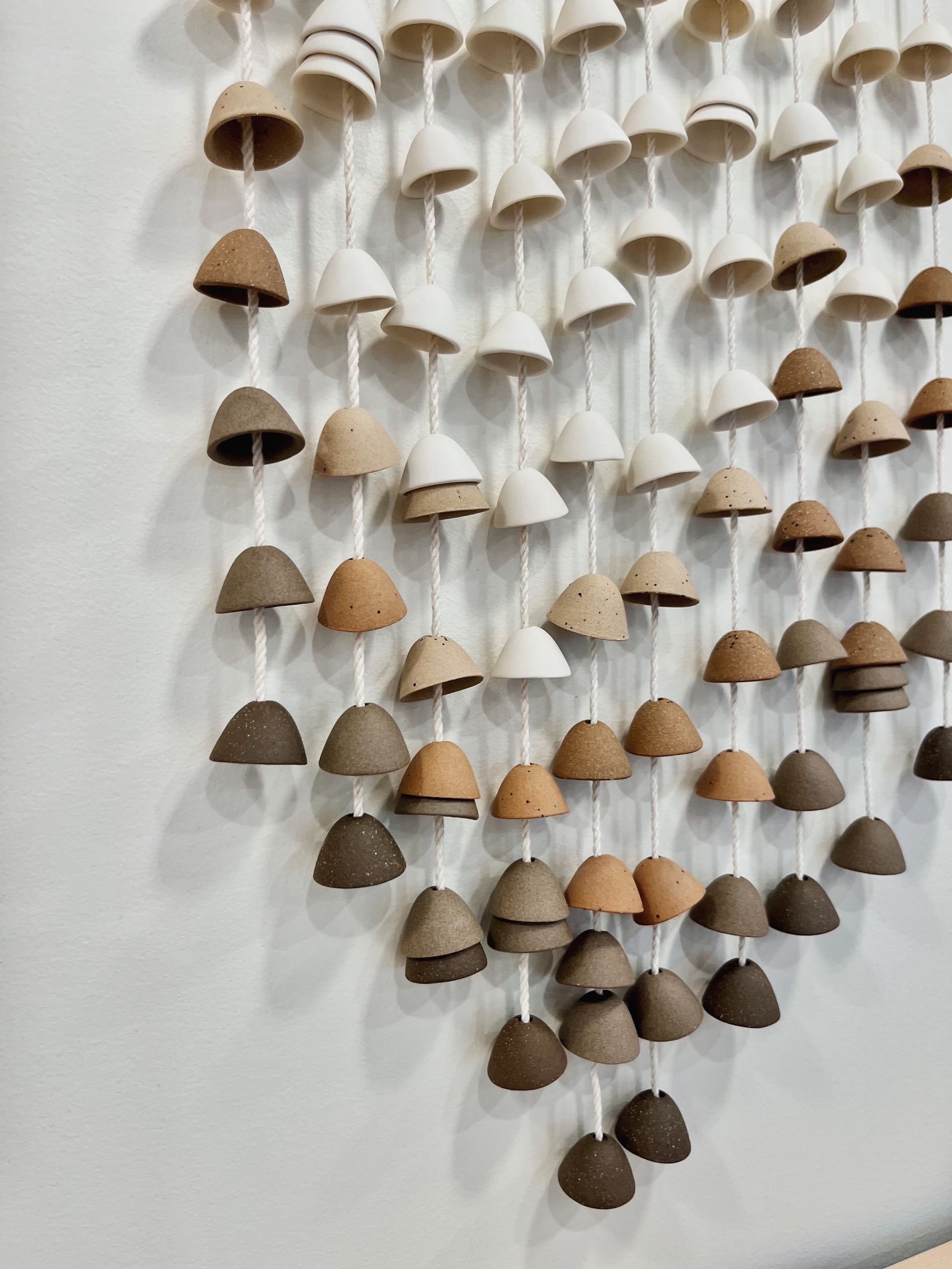 Wall hanging of small cone-shaped ornaments in white and tan, clustered on a light background