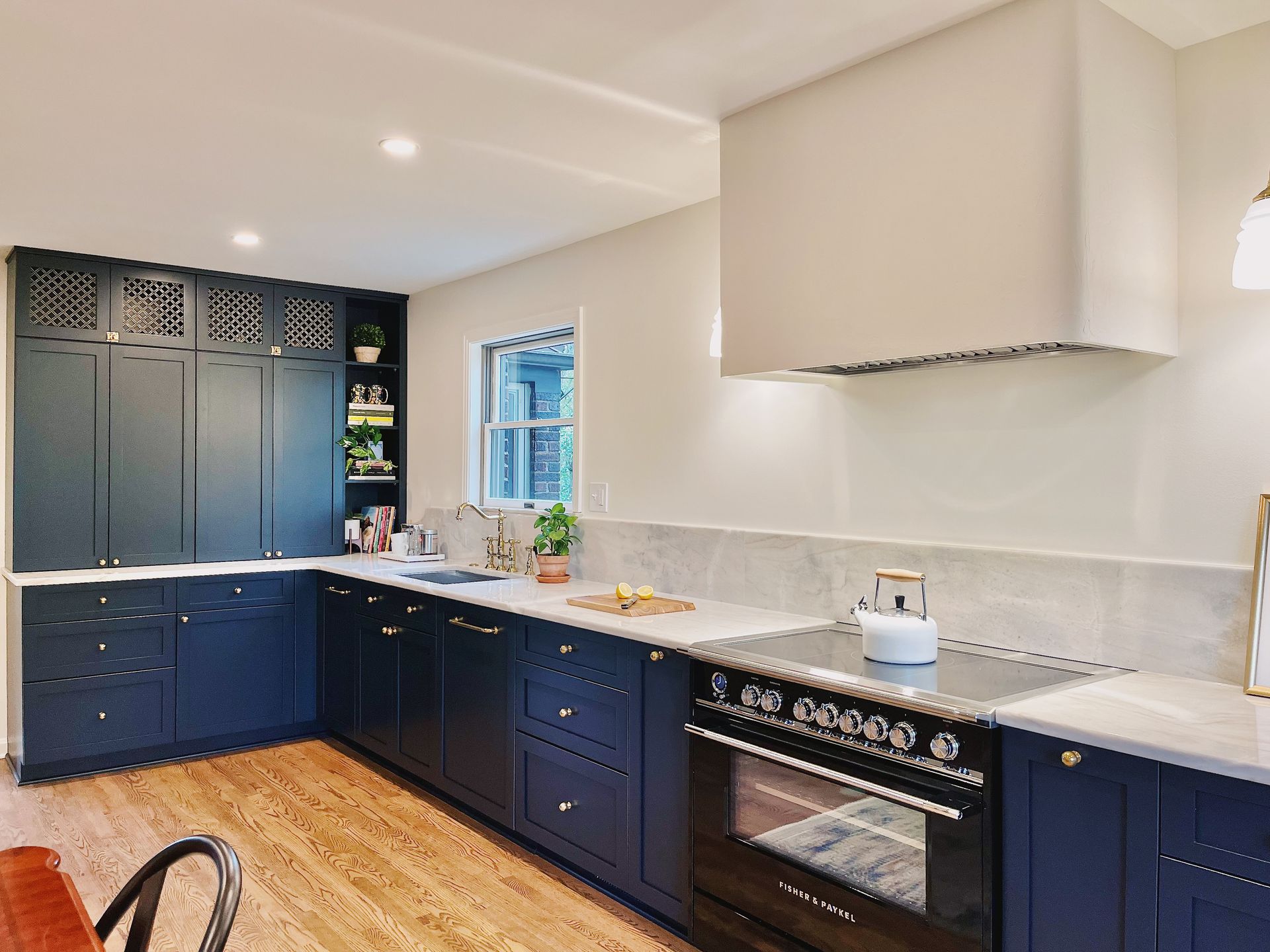 Modern kitchen with navy cabinets, white countertops, and a black stove under a large hood