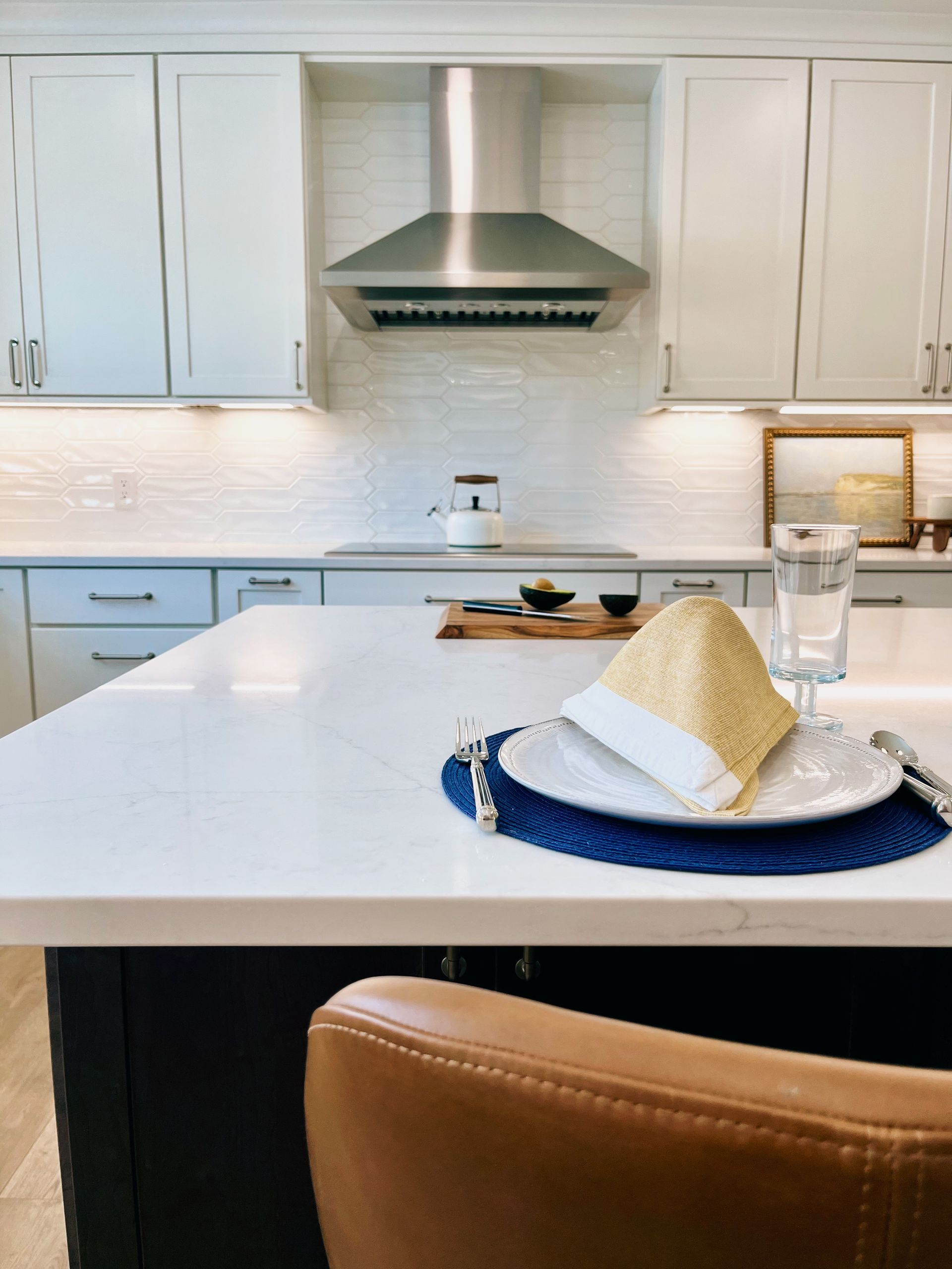Bright white kitchen with island, blue placemat, and stainless steel range hood