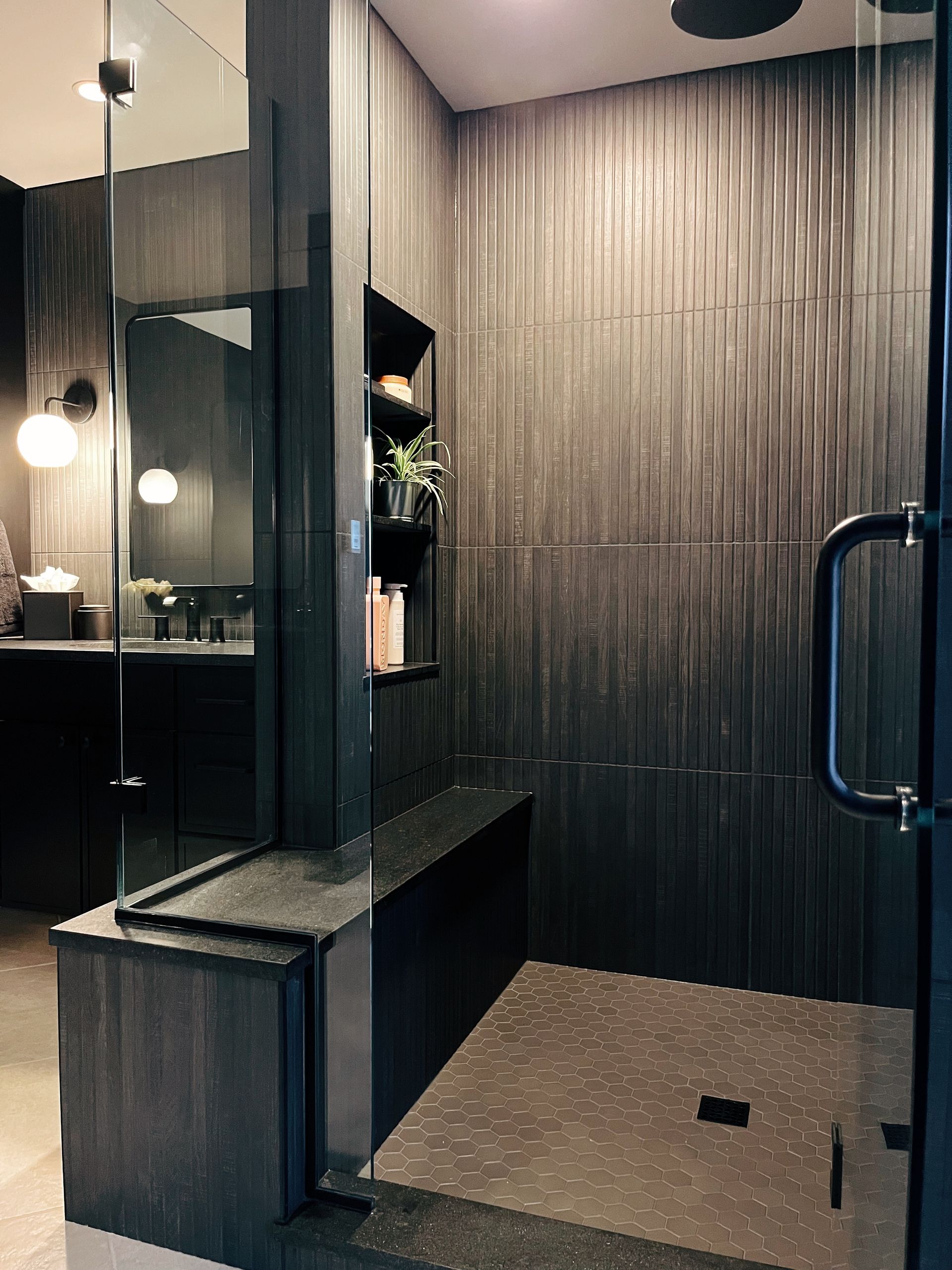 Modern shower room with black glass, gray tile walls, and a stone-textured floor mat.