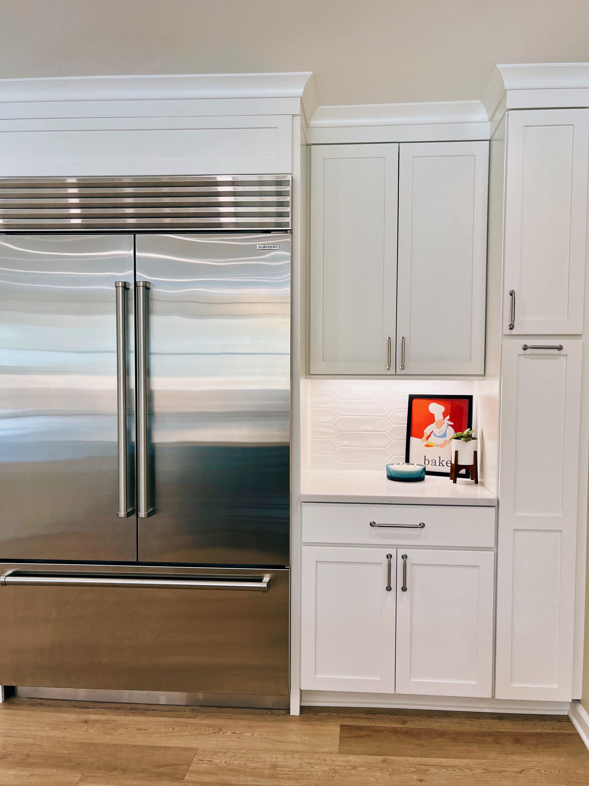 White kitchen with stainless steel refrigerator, white cabinets, and a small lit counter display.