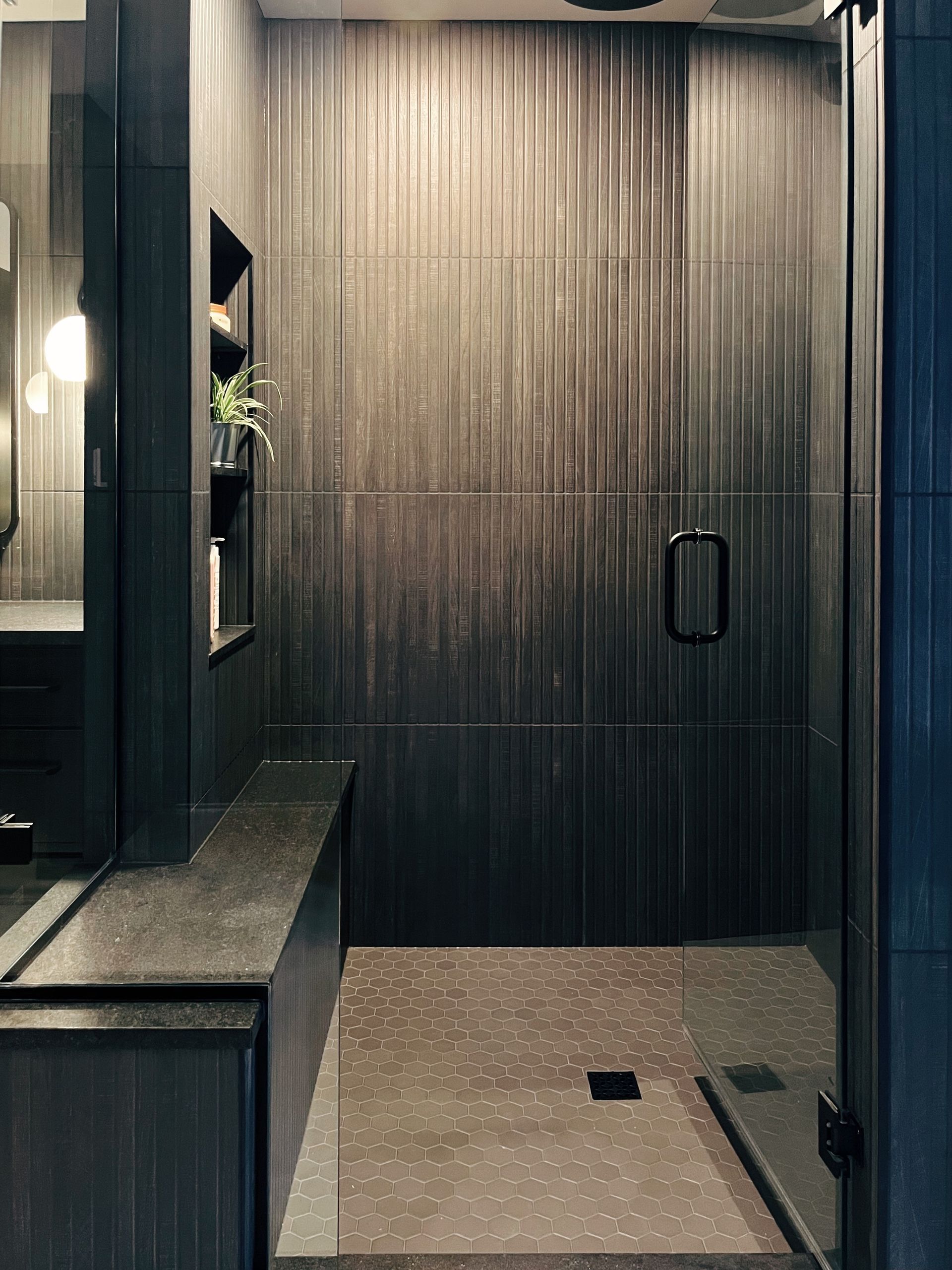 Modern dark wood shower stall with glass door and tiled floor in a compact bathroom