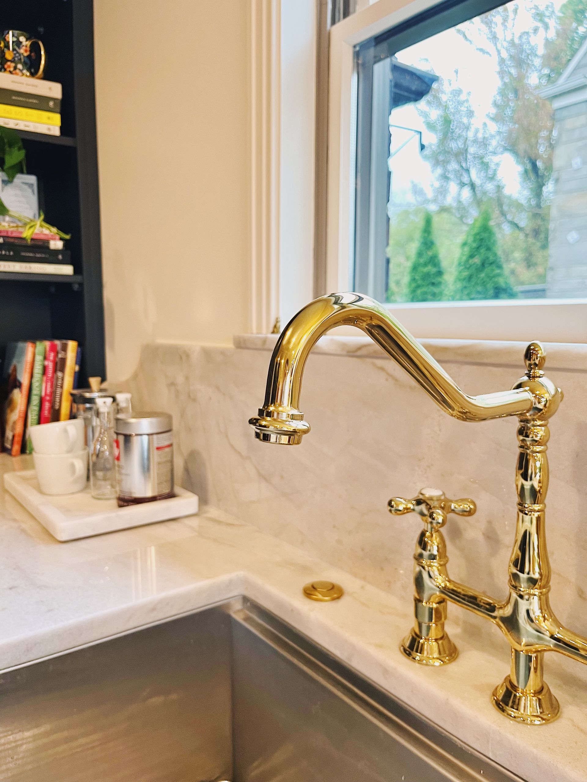 Kitchen sink with brass faucet and soap dispenser beside a window