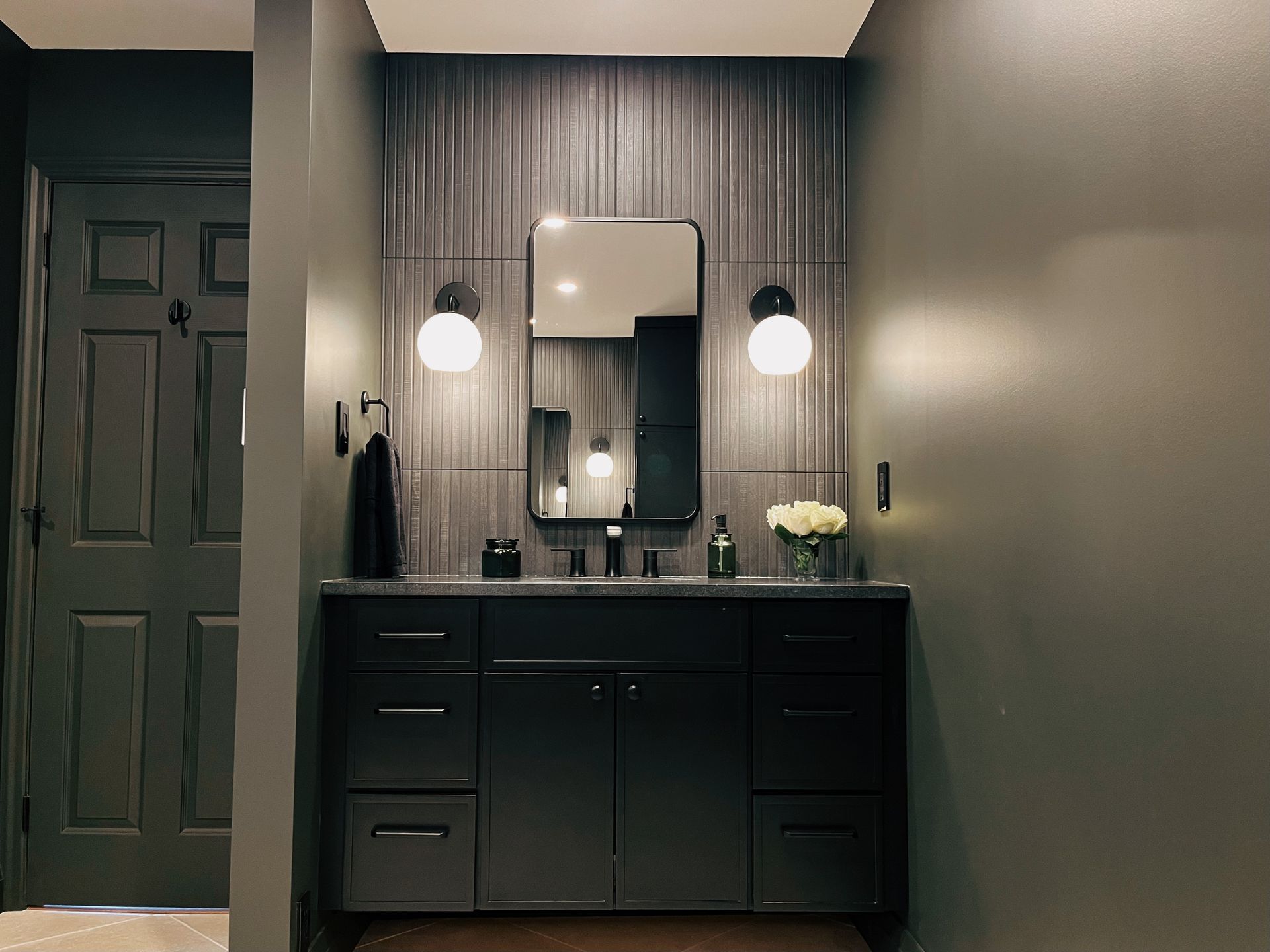 Modern bathroom vanity with dark cabinets, round lights, and a mirror against gray walls.
