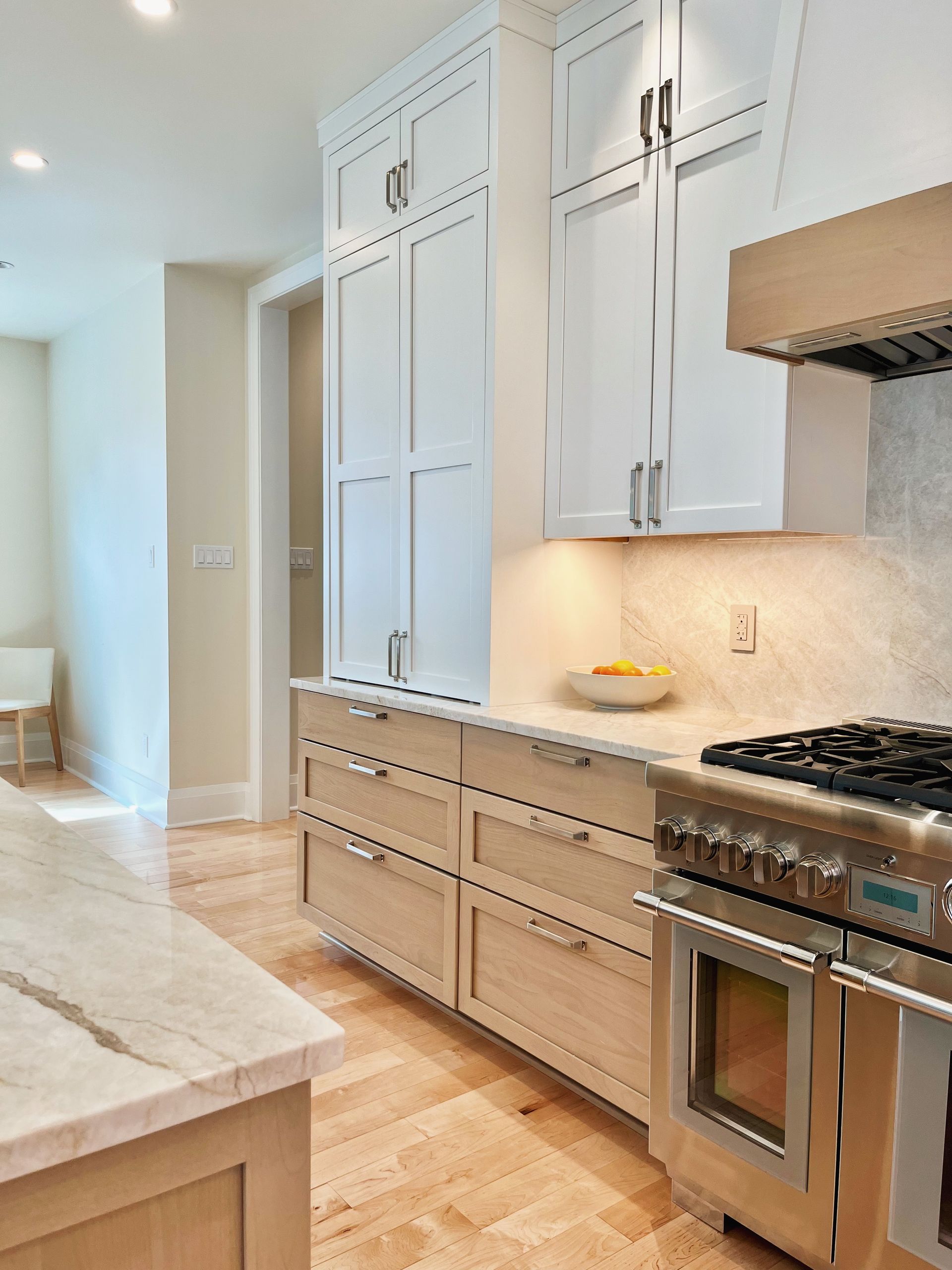 Modern kitchen with white cabinets, marble island, and stainless steel oven on herringbone wood floor